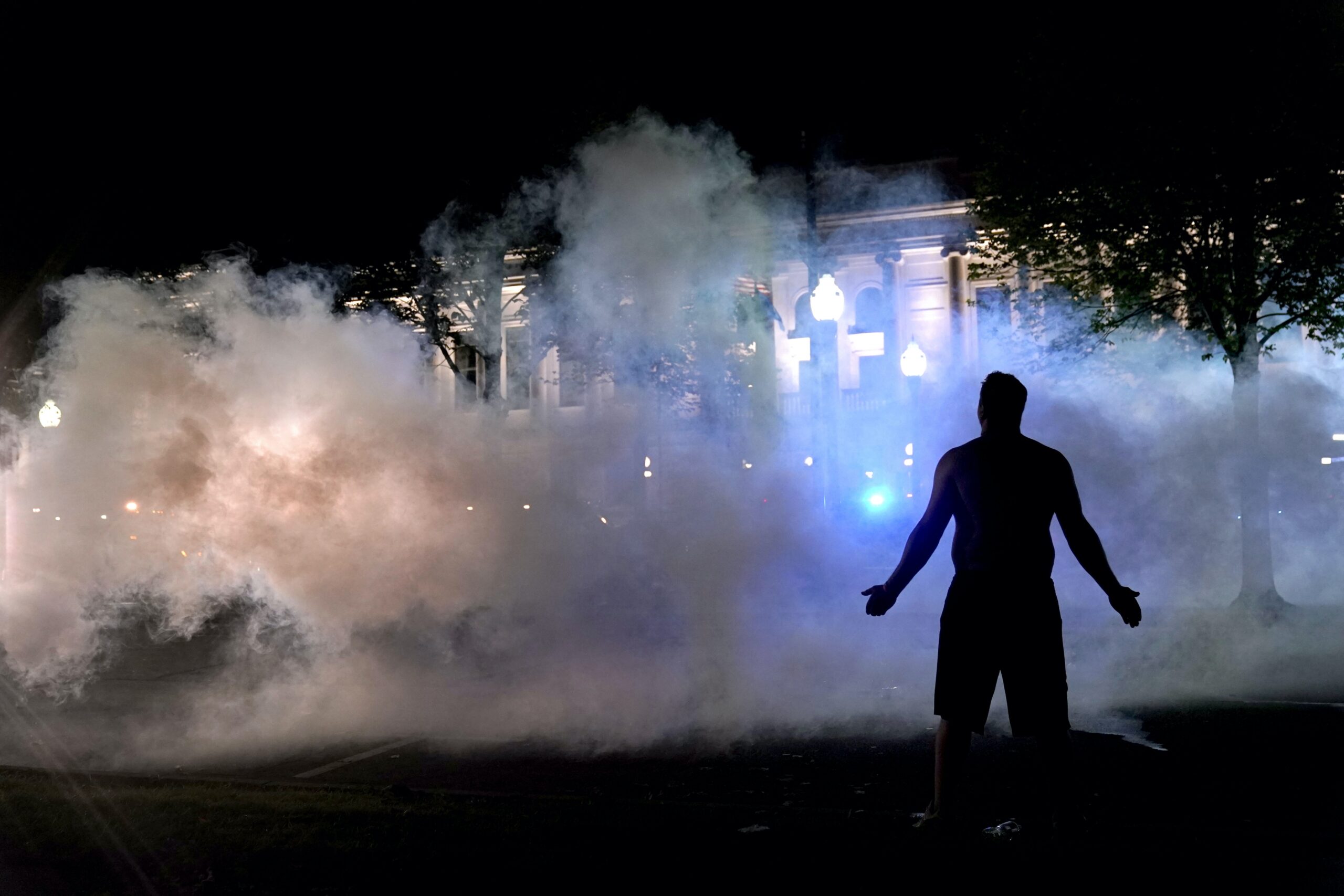 A protester attempts to continue standing through a cloud of tear gas fired by Kenosha police.