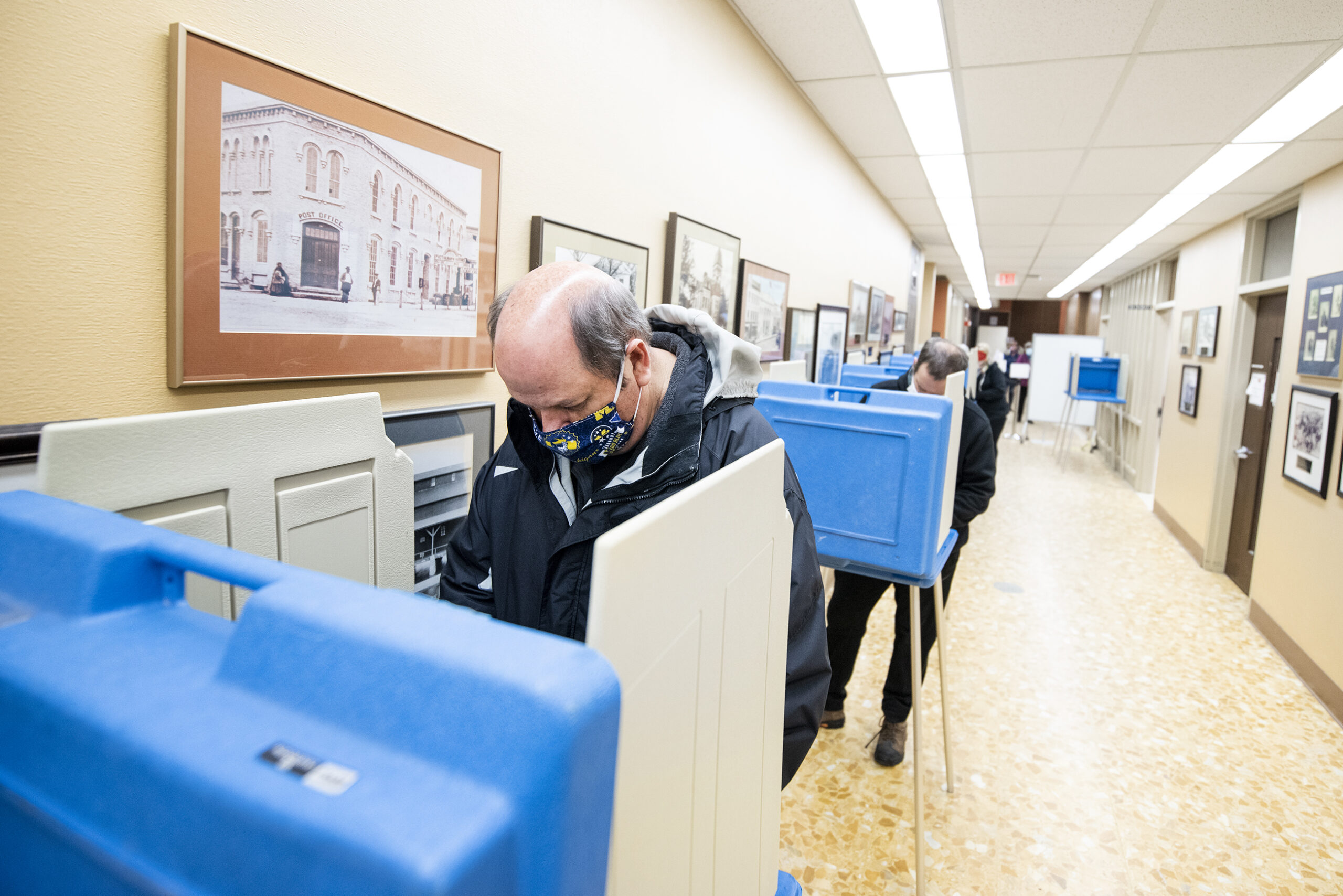 A man in a face mask stands at voting booth to fill out a ballot