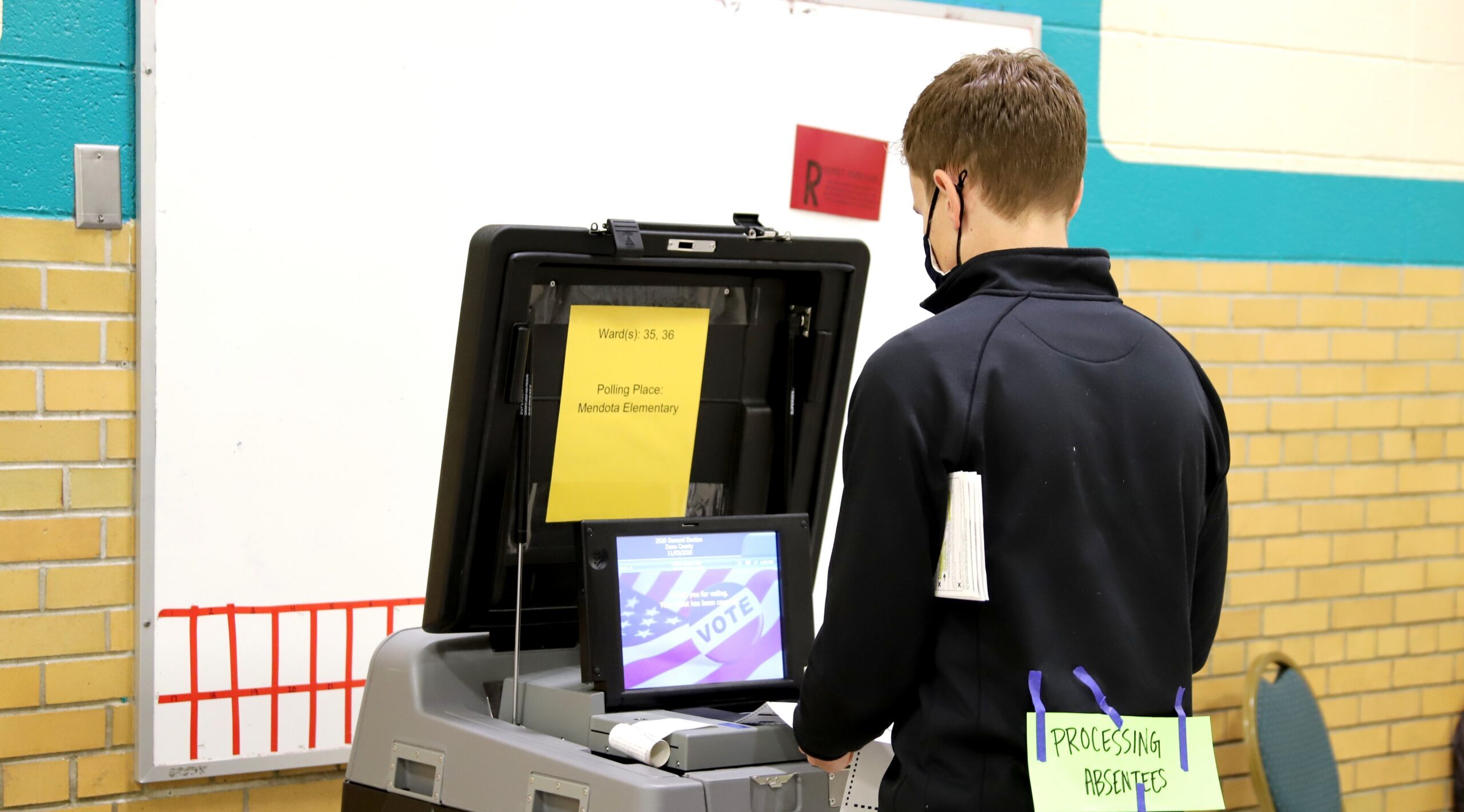 A poll worker inserts absentee ballots into a voting machine at Mendota Elementary School on Madison's north side