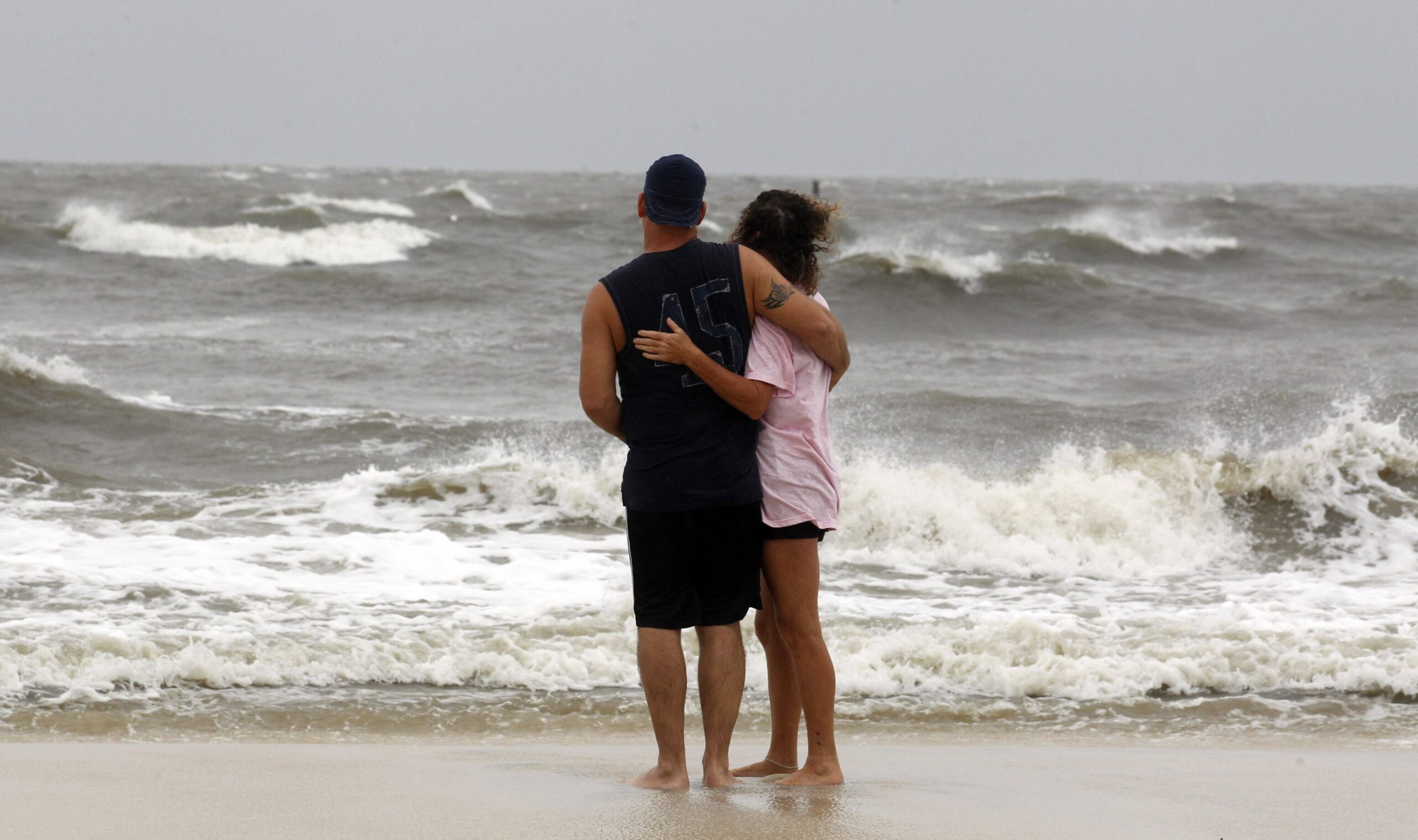 A couple watches as waves break along the beach