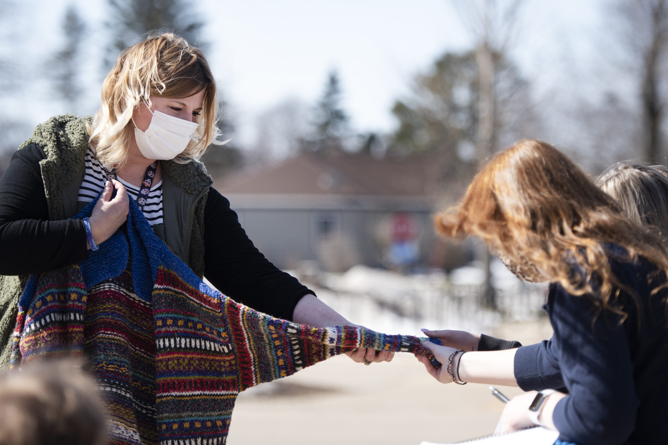 A woman in a face mask holds the arm of a sweater out to students who reach out and touch it.