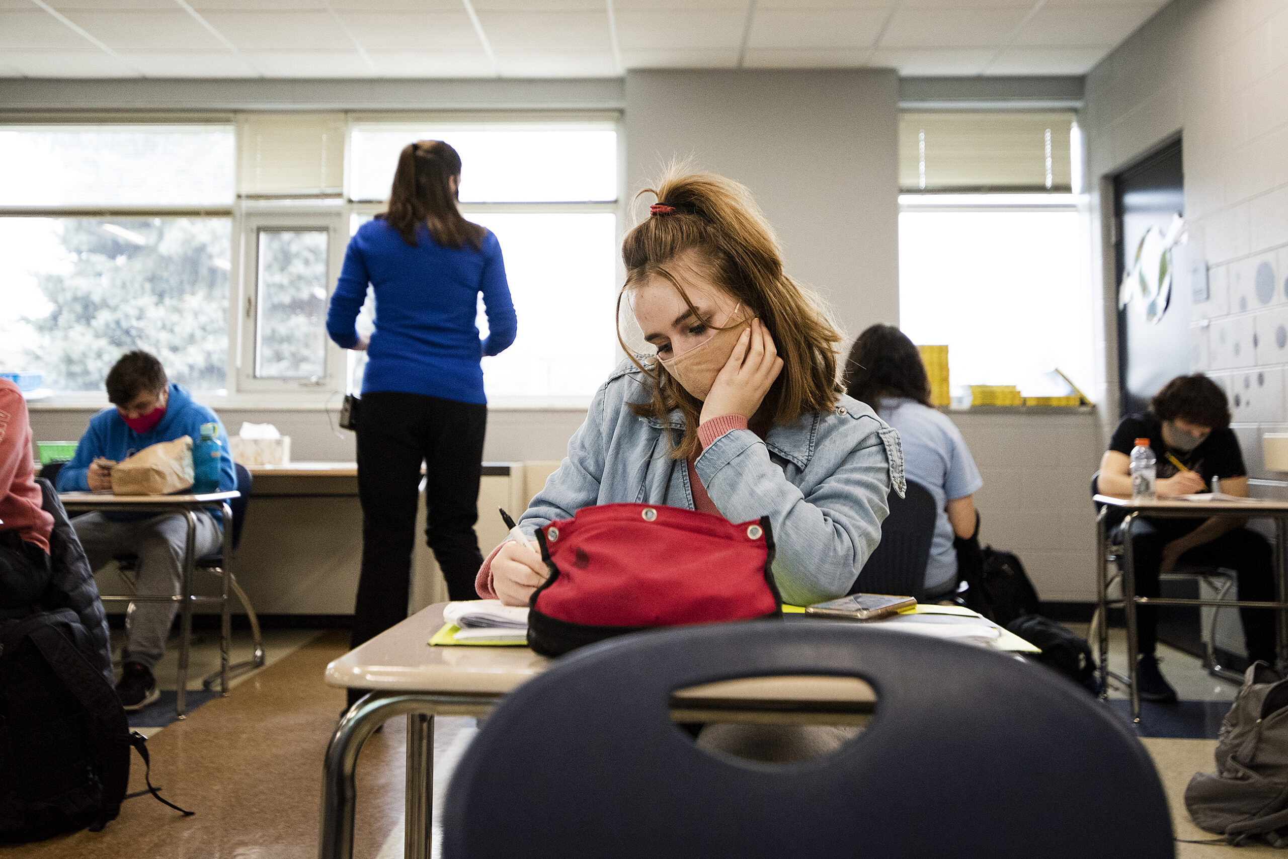 A student rests her head in her hand as she works on classwork at a desk.