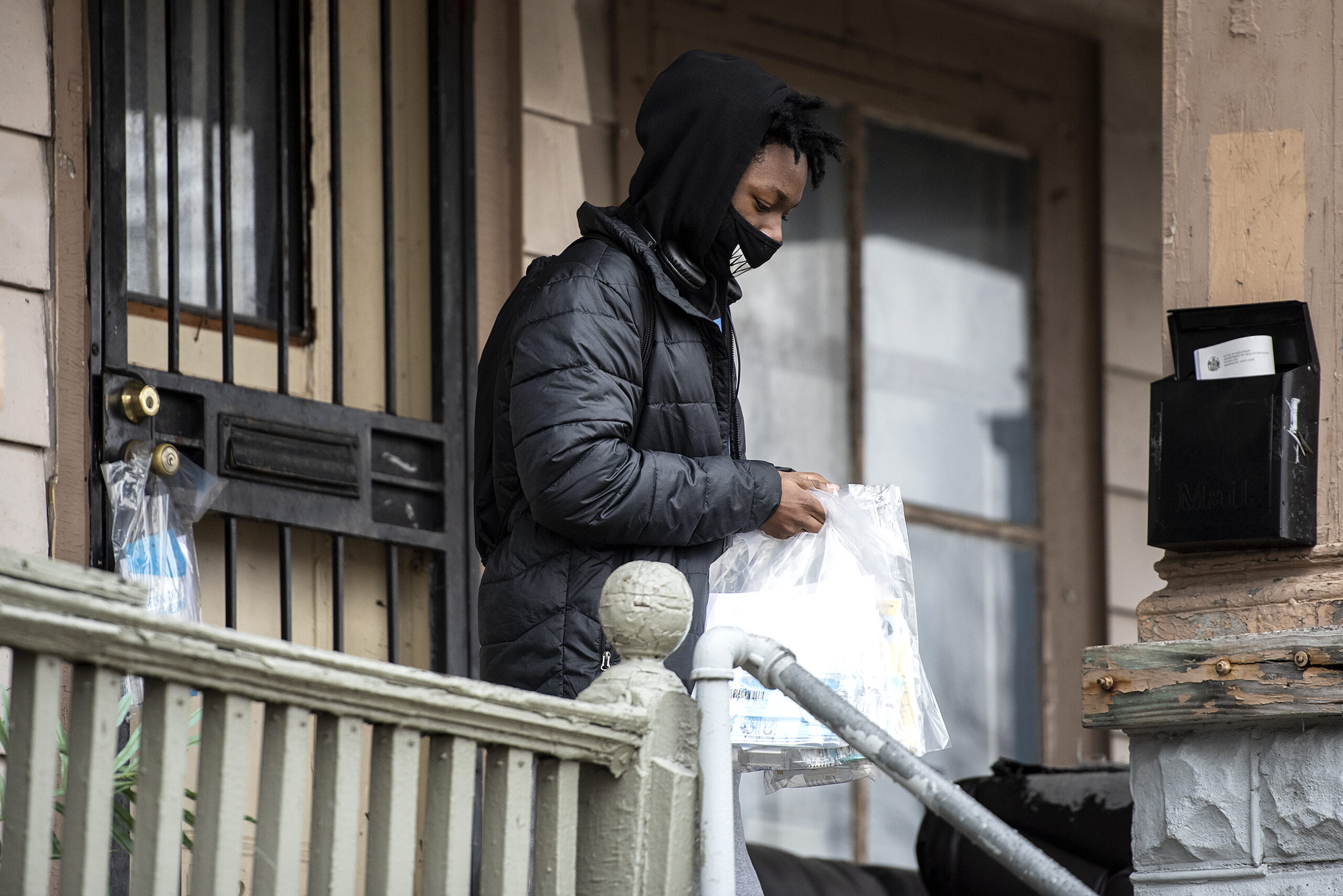 A person carries plastic bags as he walks away from a house's front door.