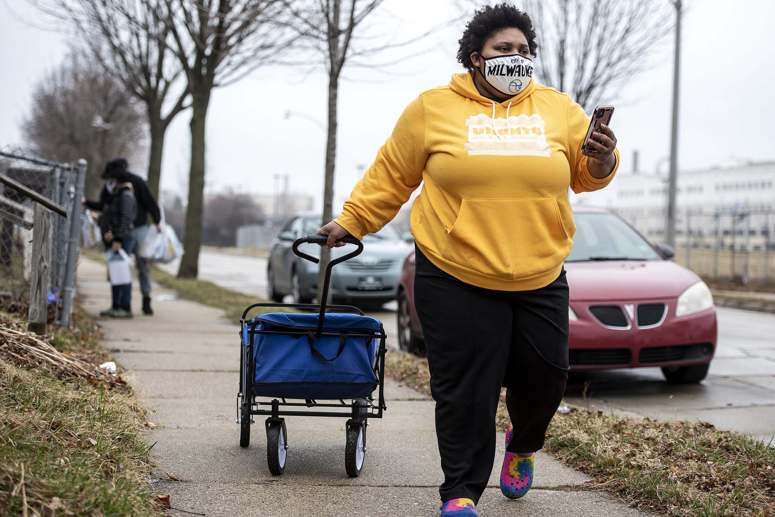 A woman pulls a wagon filled with vaccine information. She wears a face mask that says 