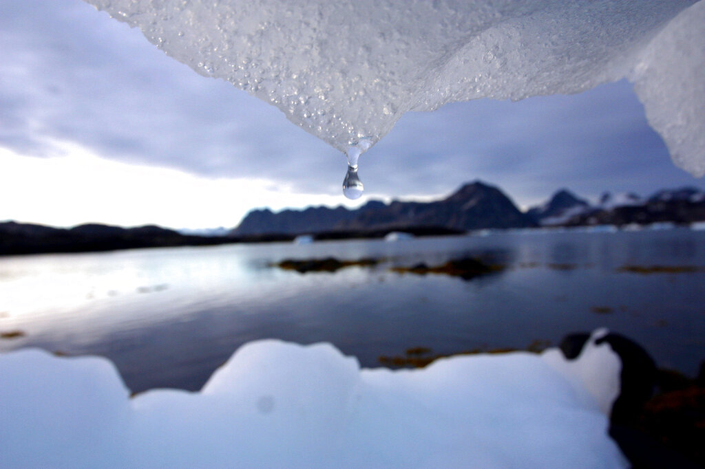 An iceberg about to let a droplet of water fall frames a view of water.