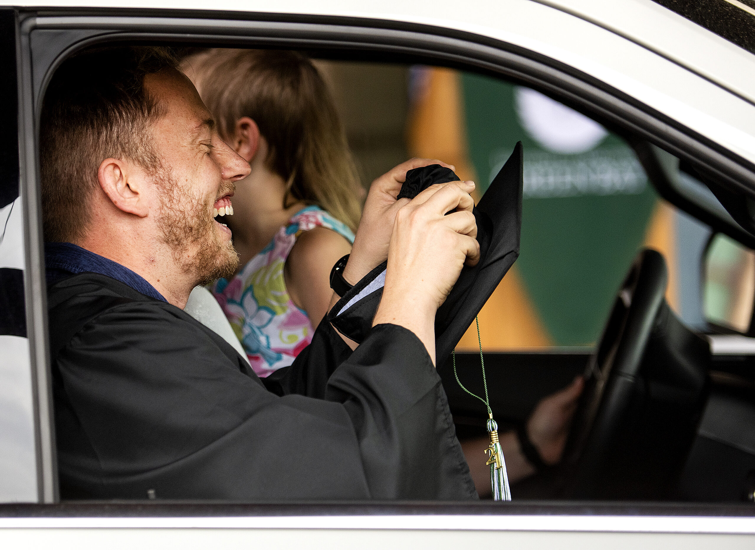 A graduate leans his head back and smiles while sitting in the passenger seat of a vehicle.