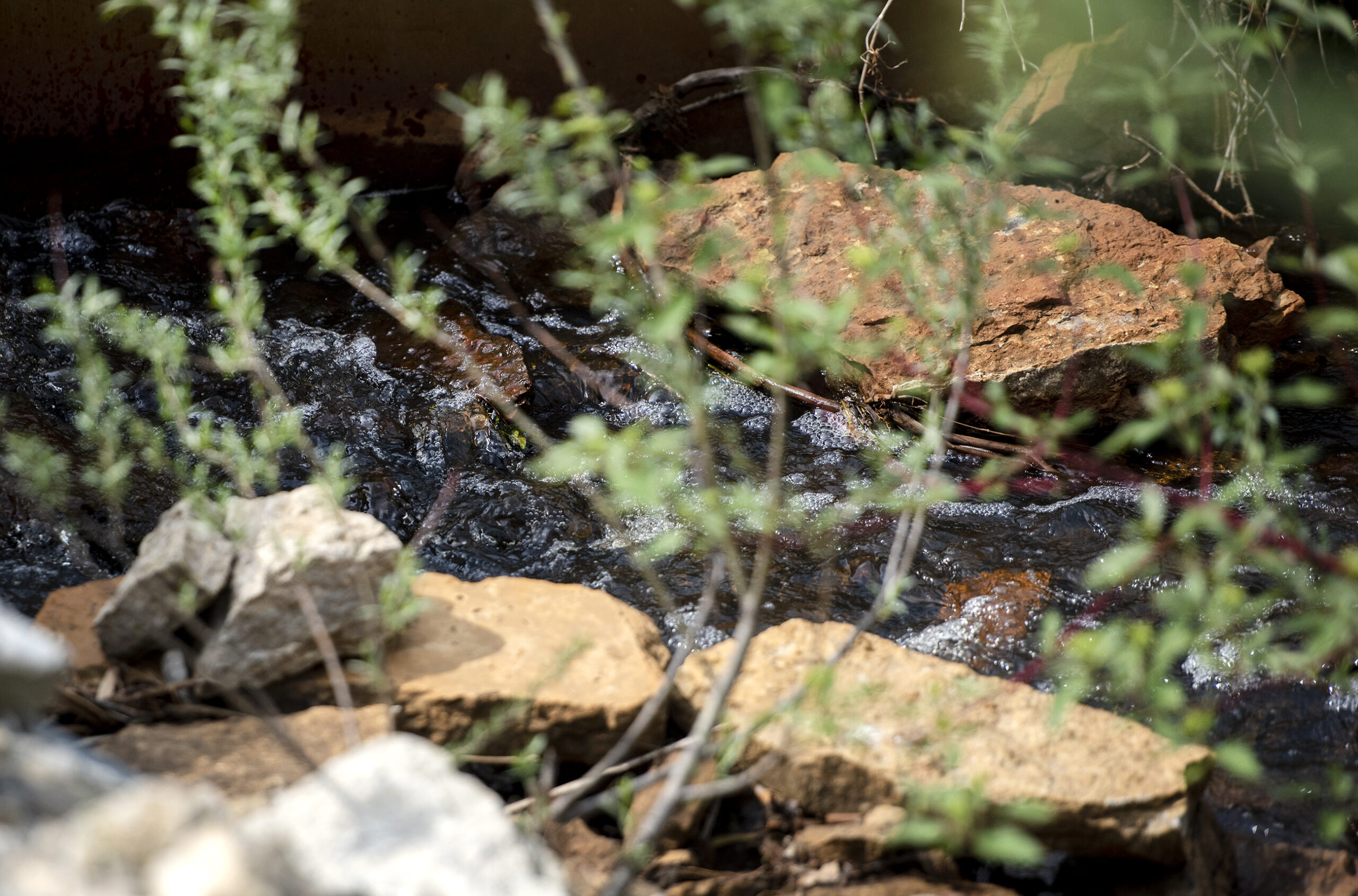 Water runs past rocks in a small ditch.