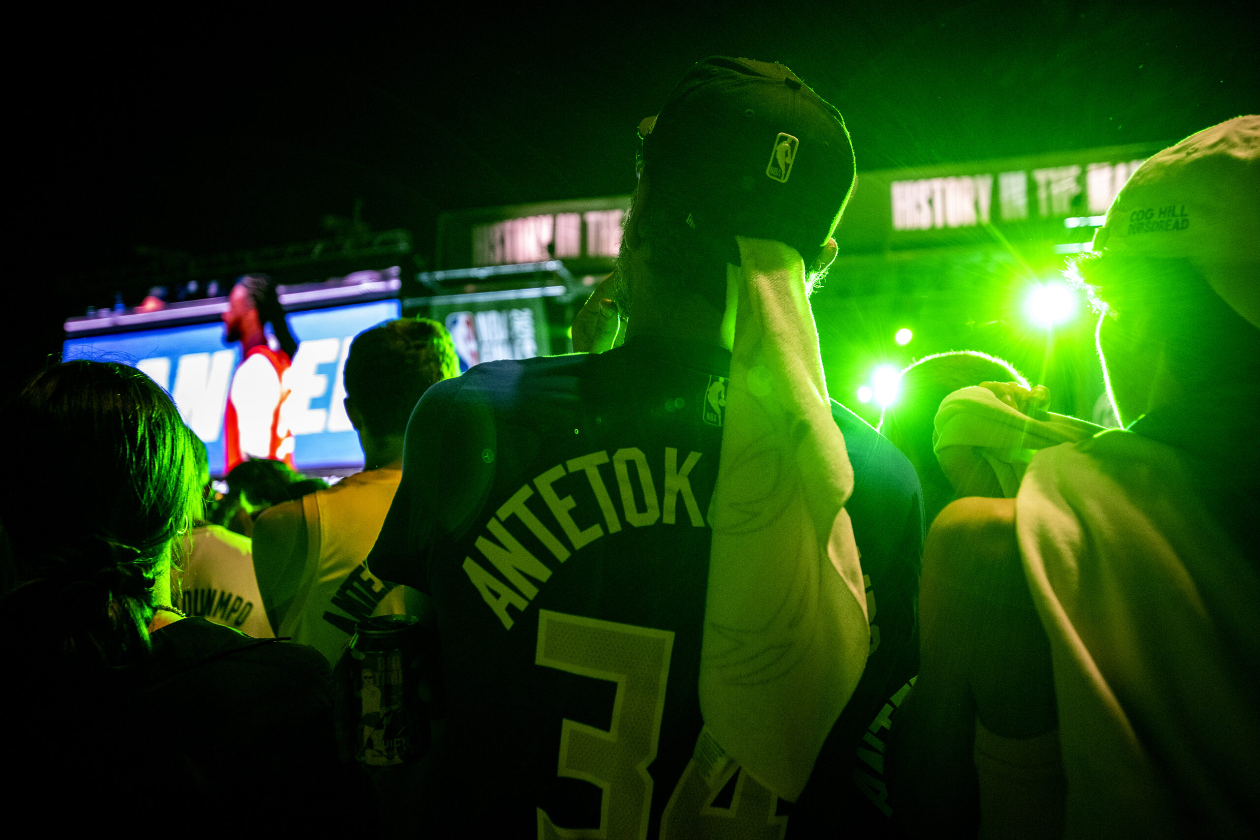 Green light shines from the stage as fans watch the game on a screen.