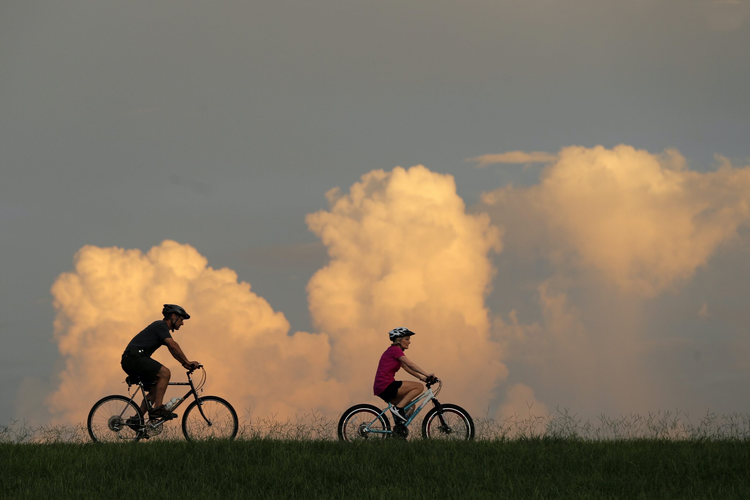 People ride bikes with cumulus clouds in the background.