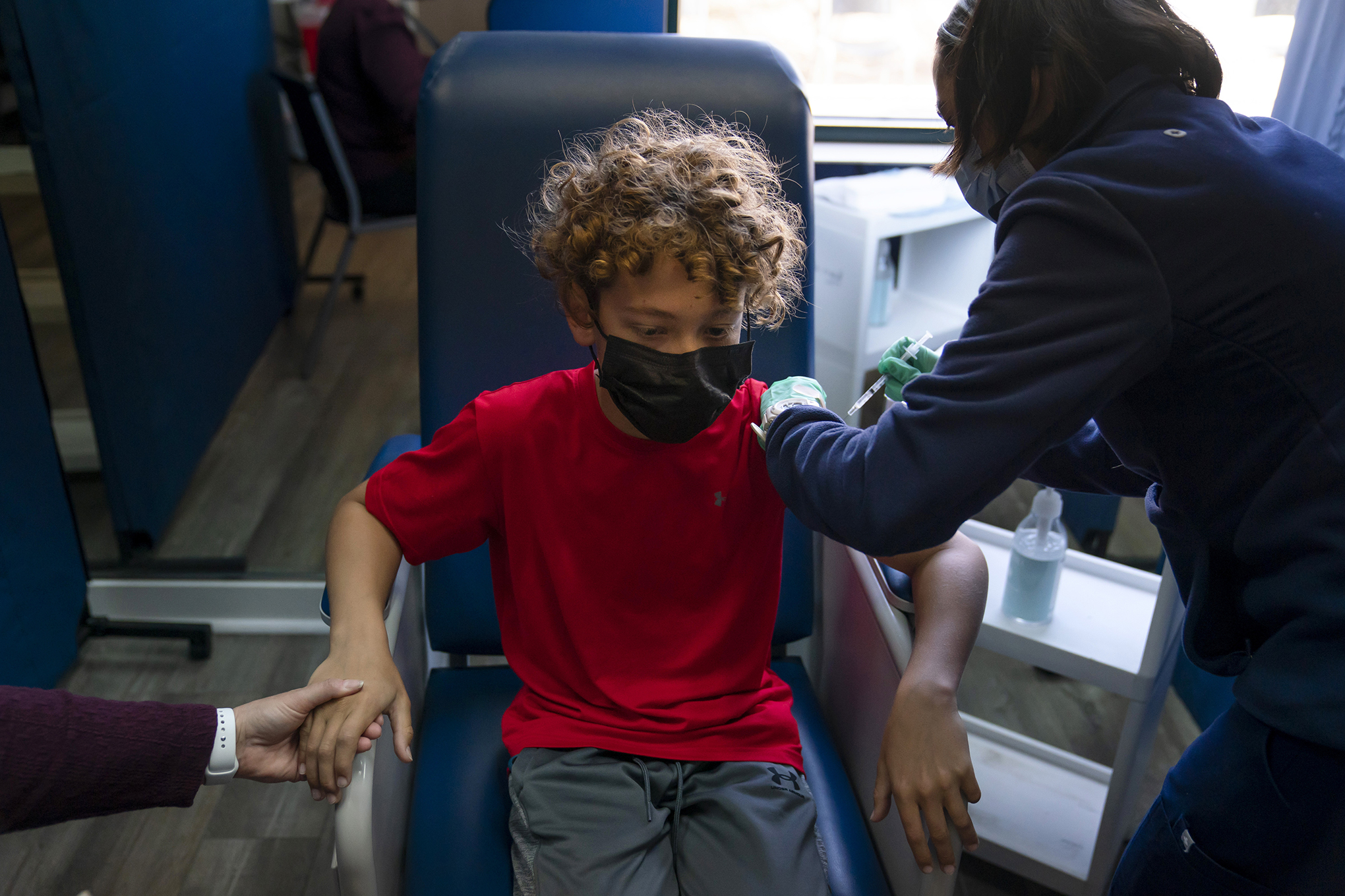 Max Cuevas, 12, holds his mother's hand as he receives the Pfizer COVID-19 vaccine
