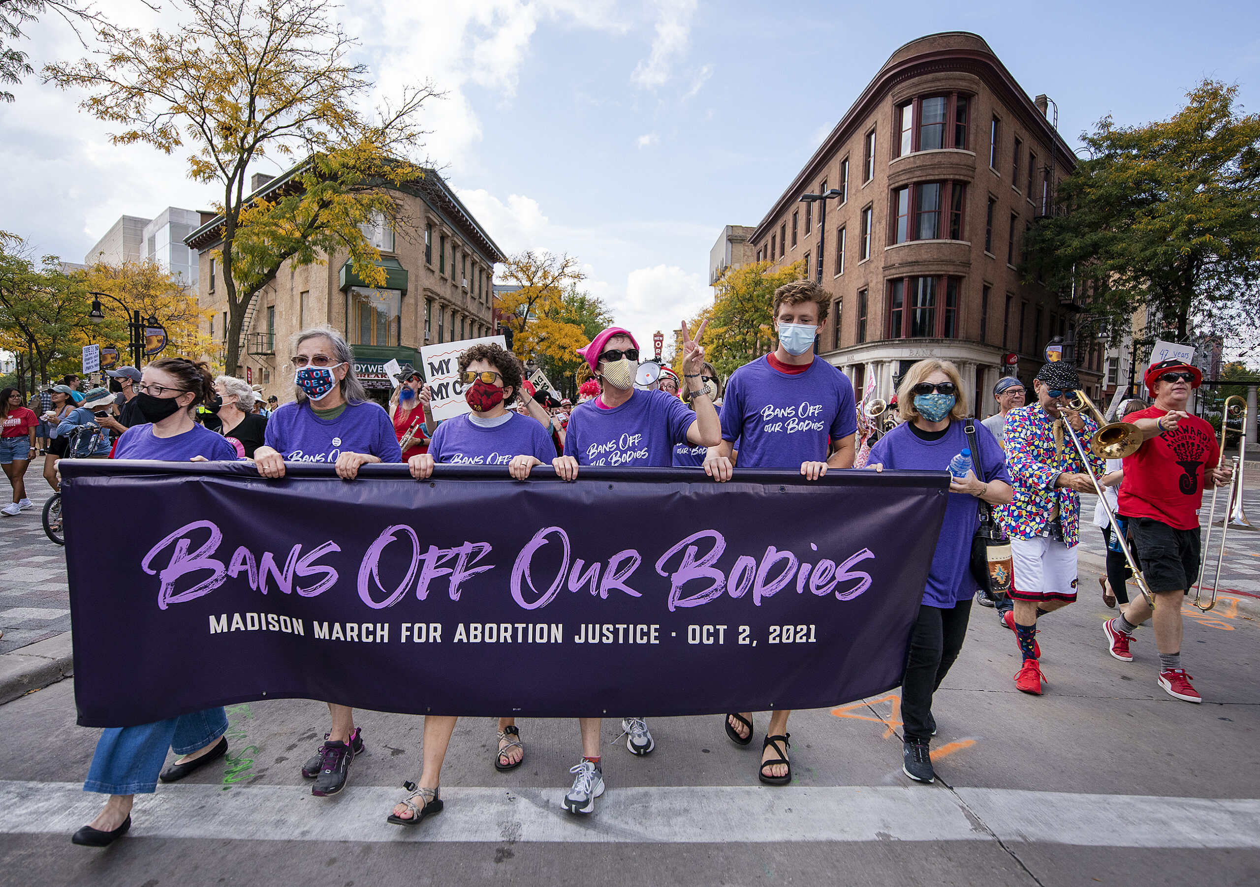 Six people hold a purple banner that says "Bans Off Our Bodies."
