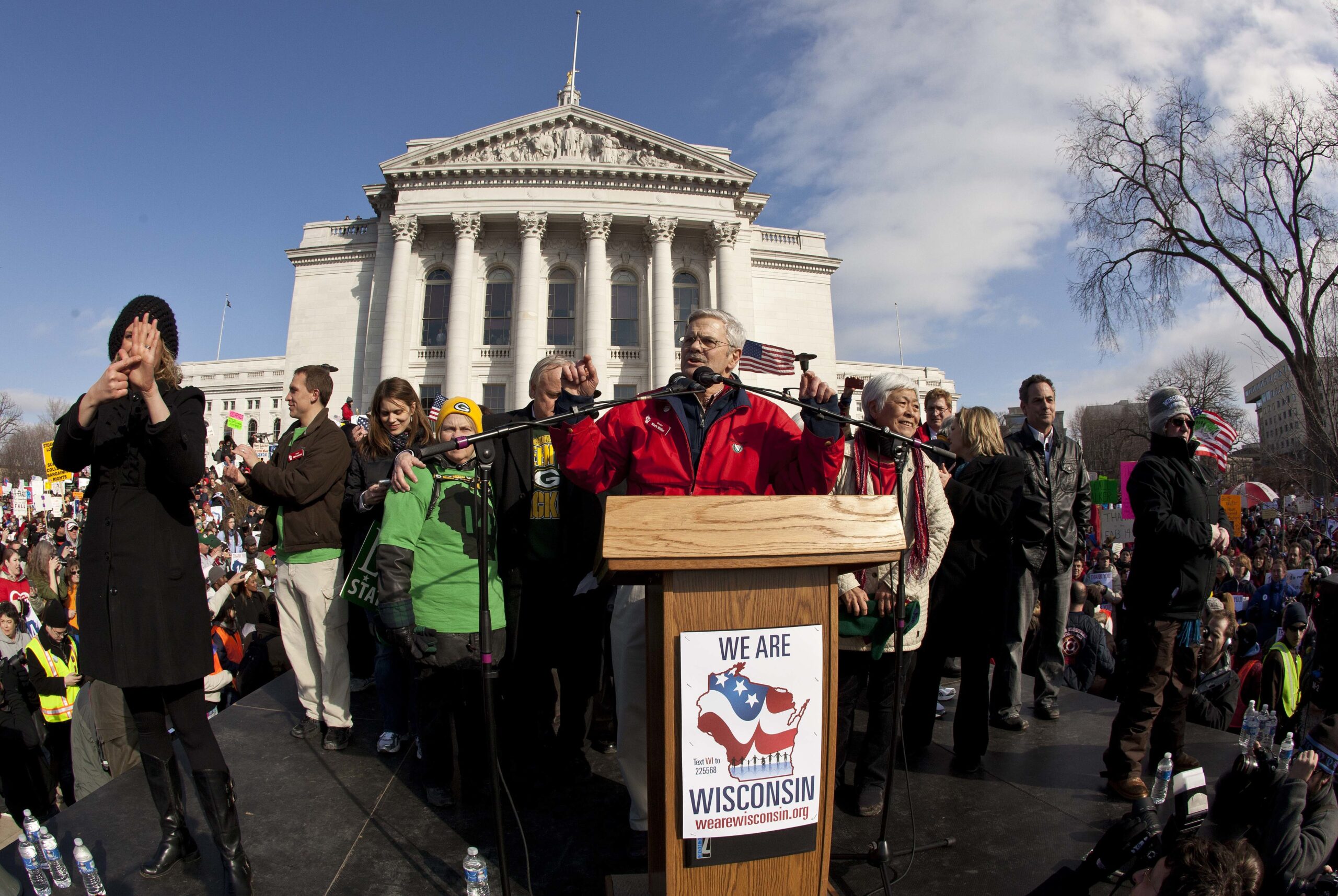 A man speaks at a podium with the Wisconsin Capitol in the background