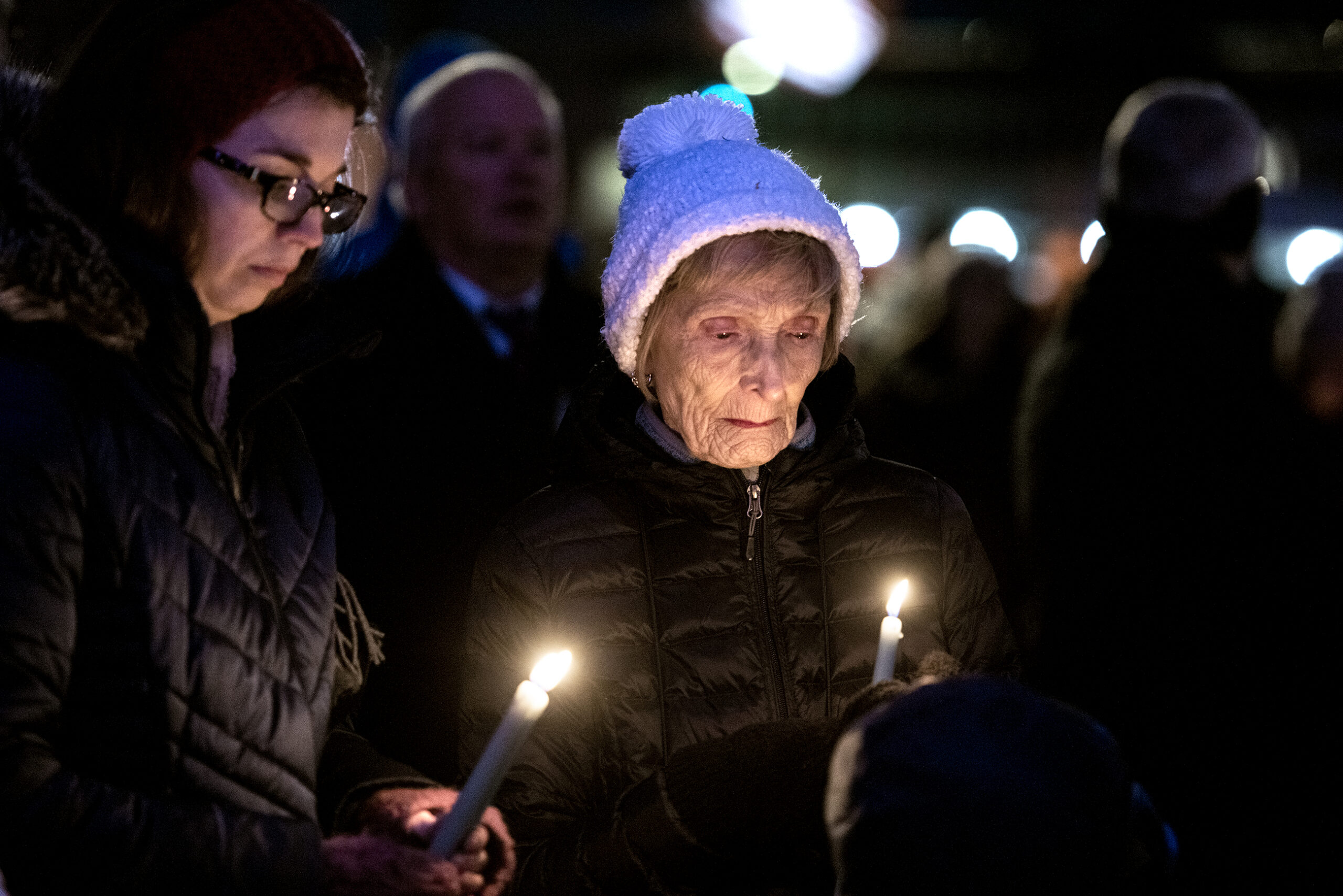 Two women hold lit candles at a vigil.