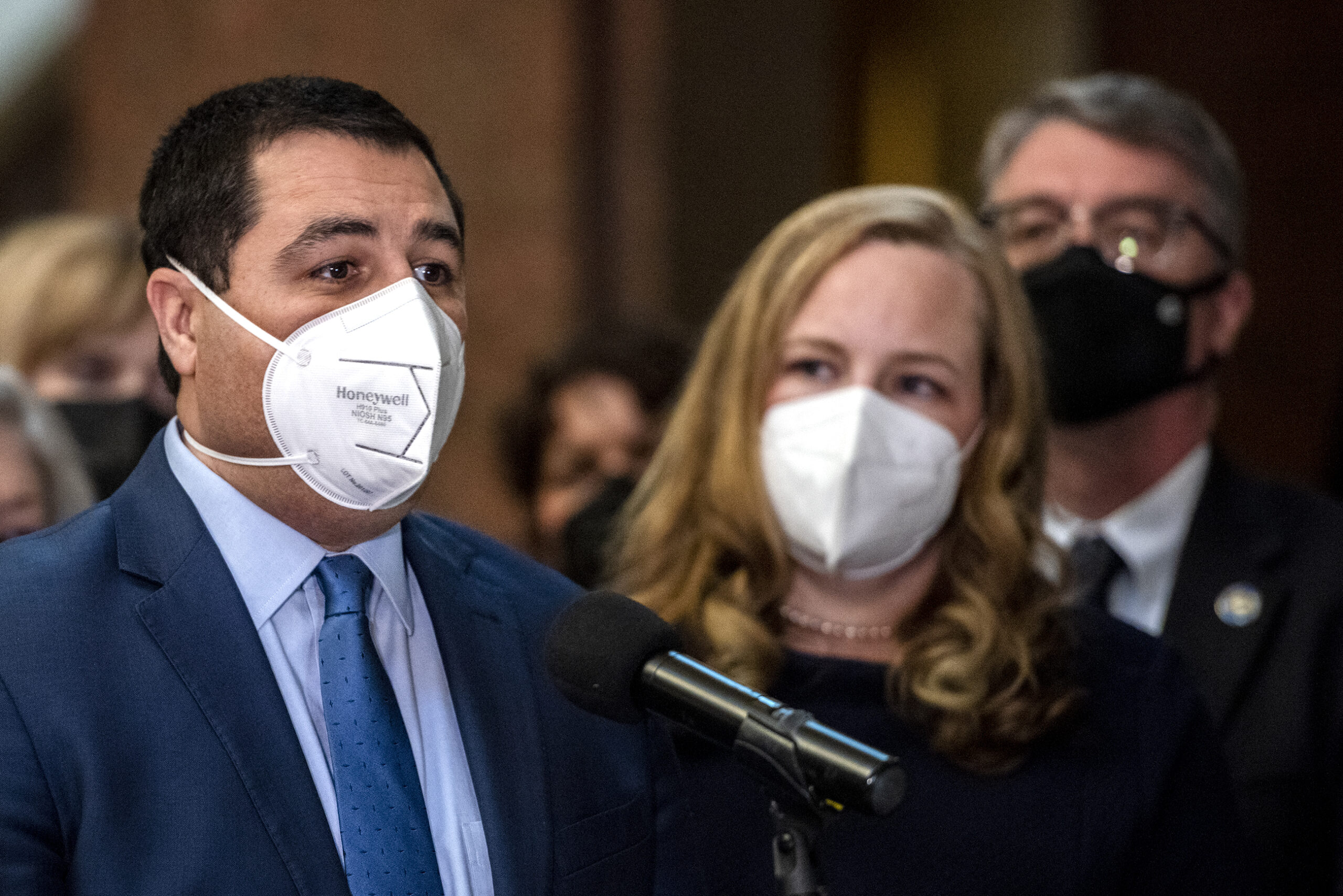 Josh Kaul wears a mask as he speaks at a podium.