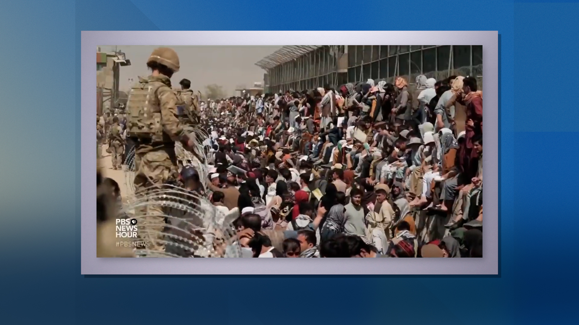 U.S. troops guard hundreds of Afghans seated and standing behind razor wire