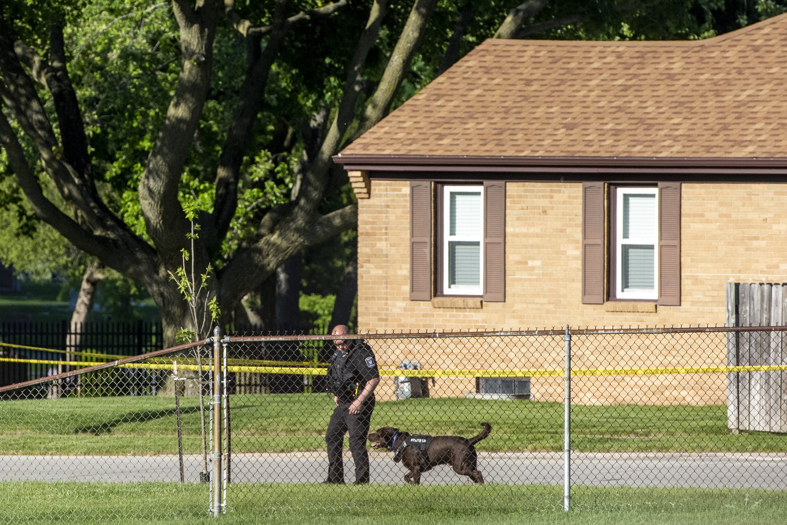 An officer and a black dog walk together near a fence.