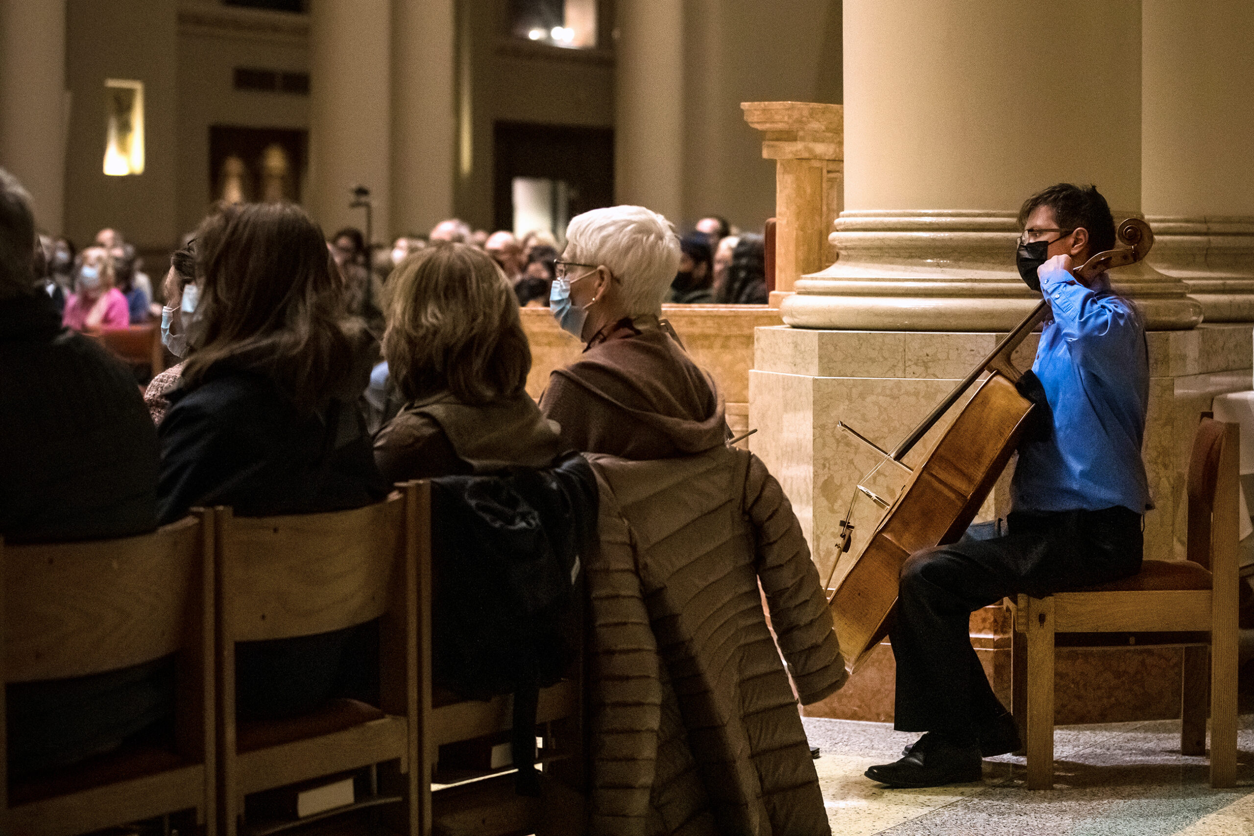 A man plays a cello among a crowd during a performance in a church