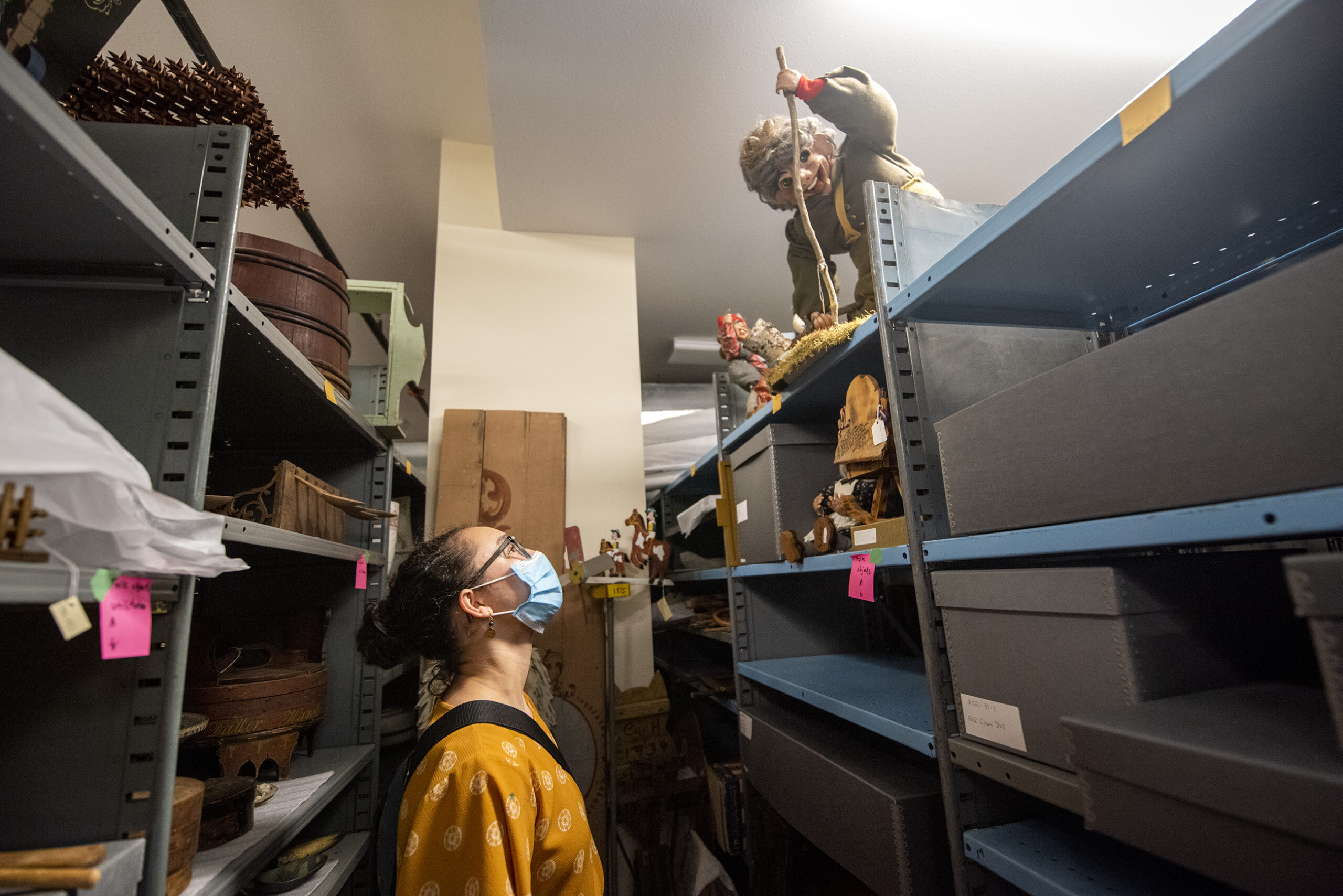 A girl looks up at a tall shelf full of museum items.