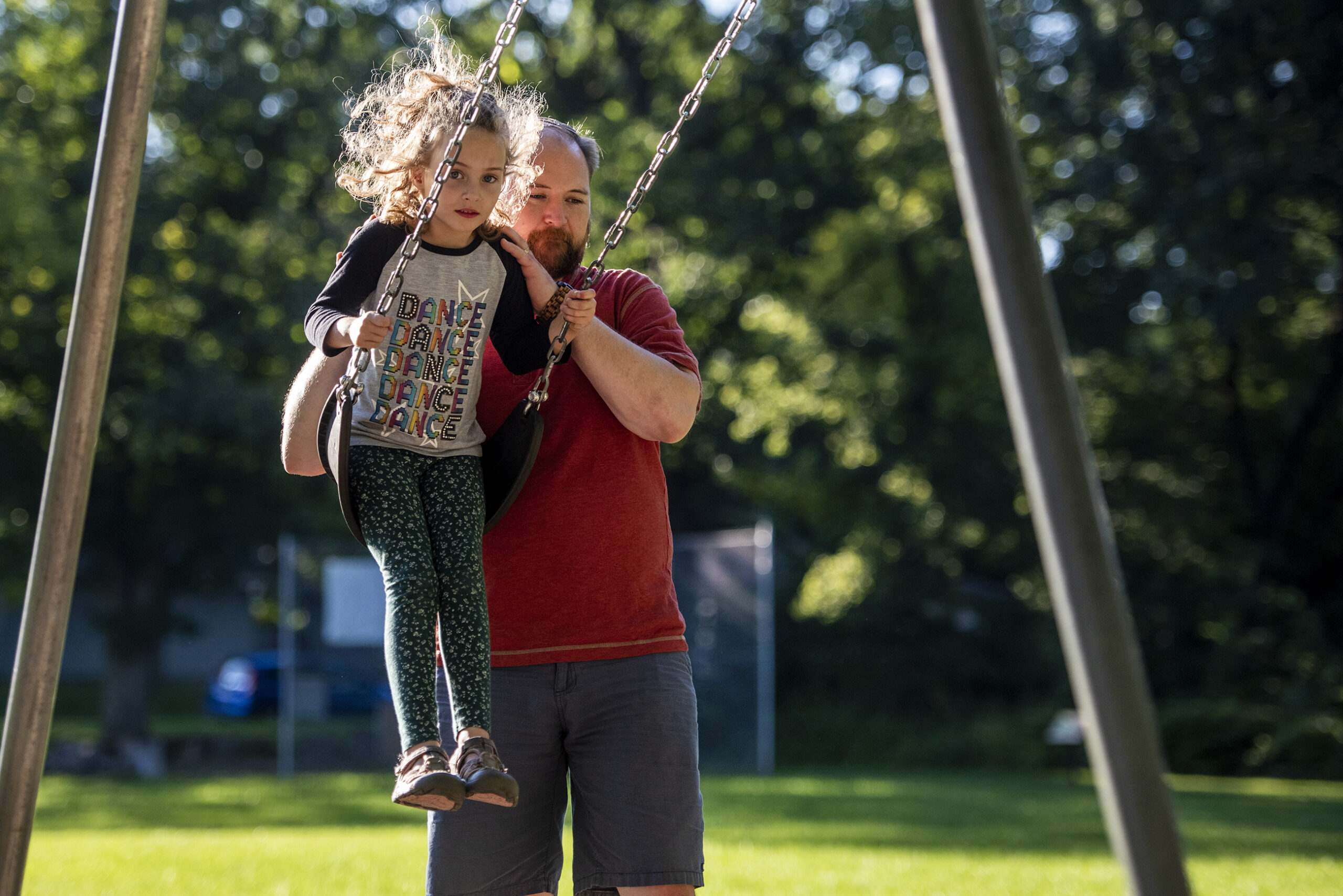 A father swings his daughter on a swing set outside.