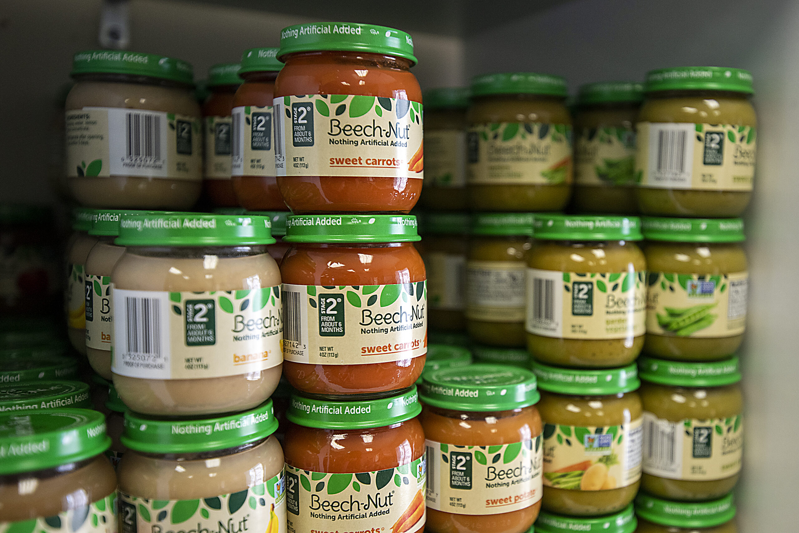 Jars of tan, orange, and green baby food are stacked on a shelf.