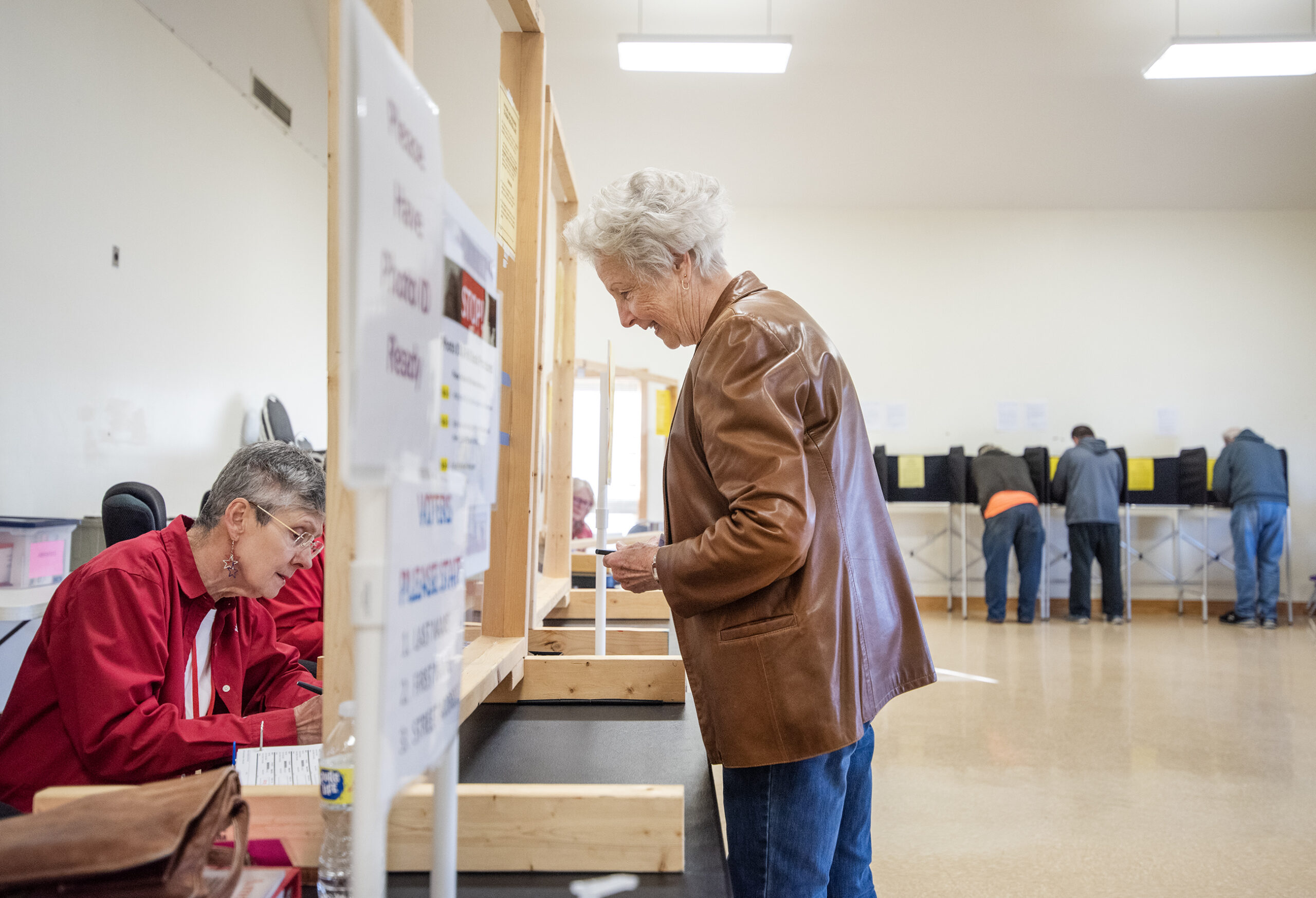 A woman in a brown leather jacket smiles as she looks at a poll worker.