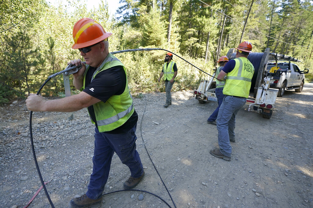Carl Roath, left, a worker with the Mason County (Wash.) Public Utility District, pulls fiber optic cable off of a spool, as he works with a team to install broadband internet service to homes in a rural area surrounding Lake Christine near Belfair, Wash.