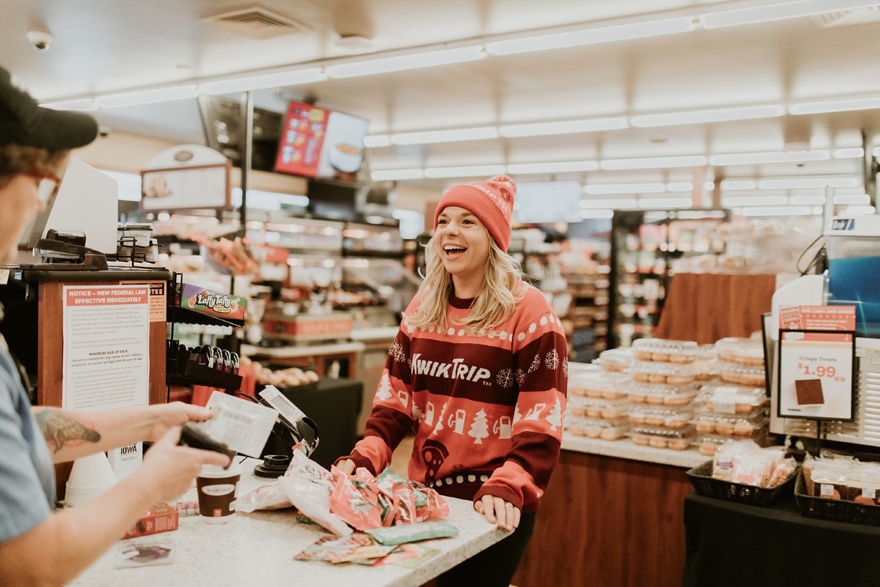 Cassandra Berger stands at the counter at Kwik Trip, wearing a Kwik Trip sweater and hat