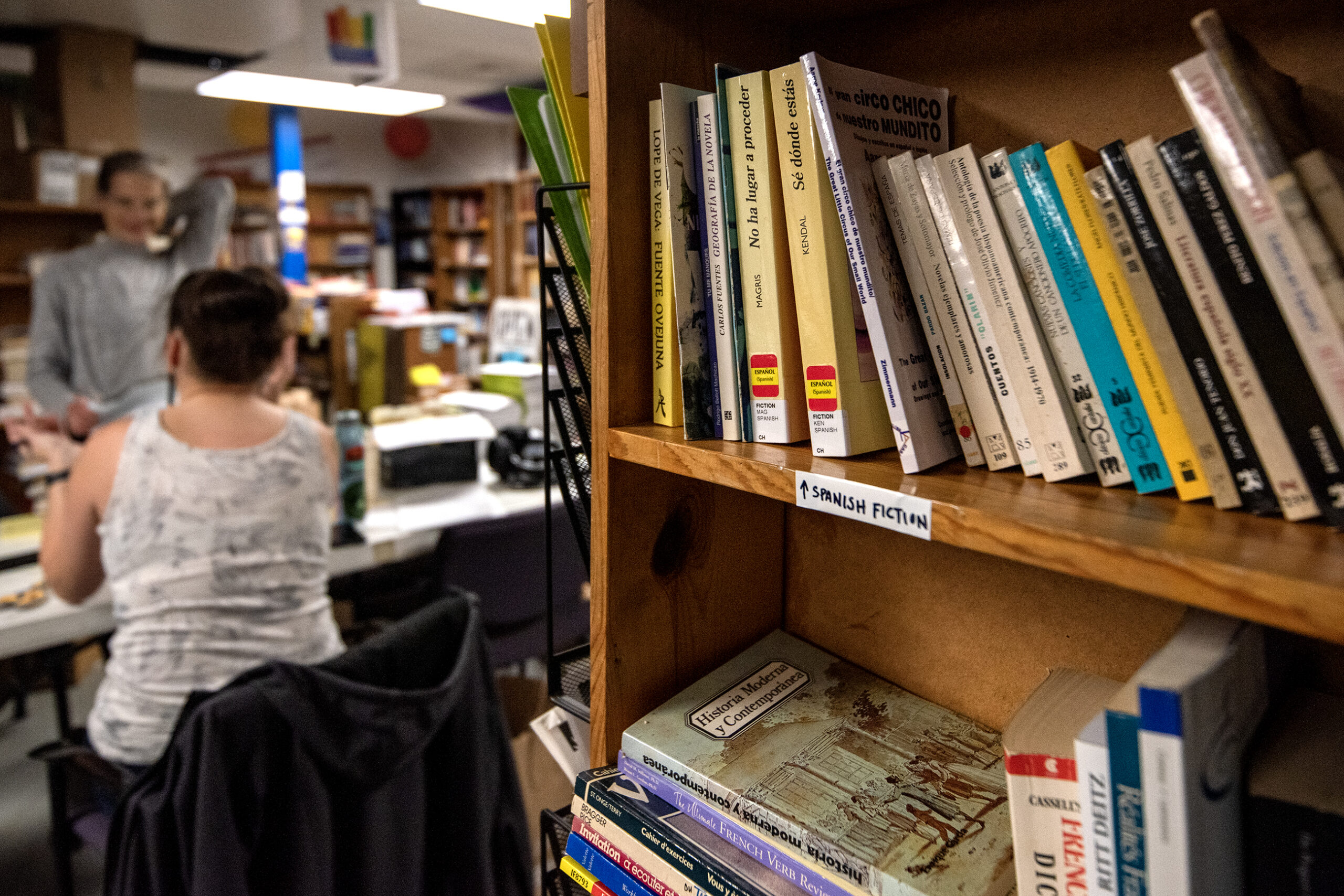 A bookshelf is stocked with books in a room where volunteers work.