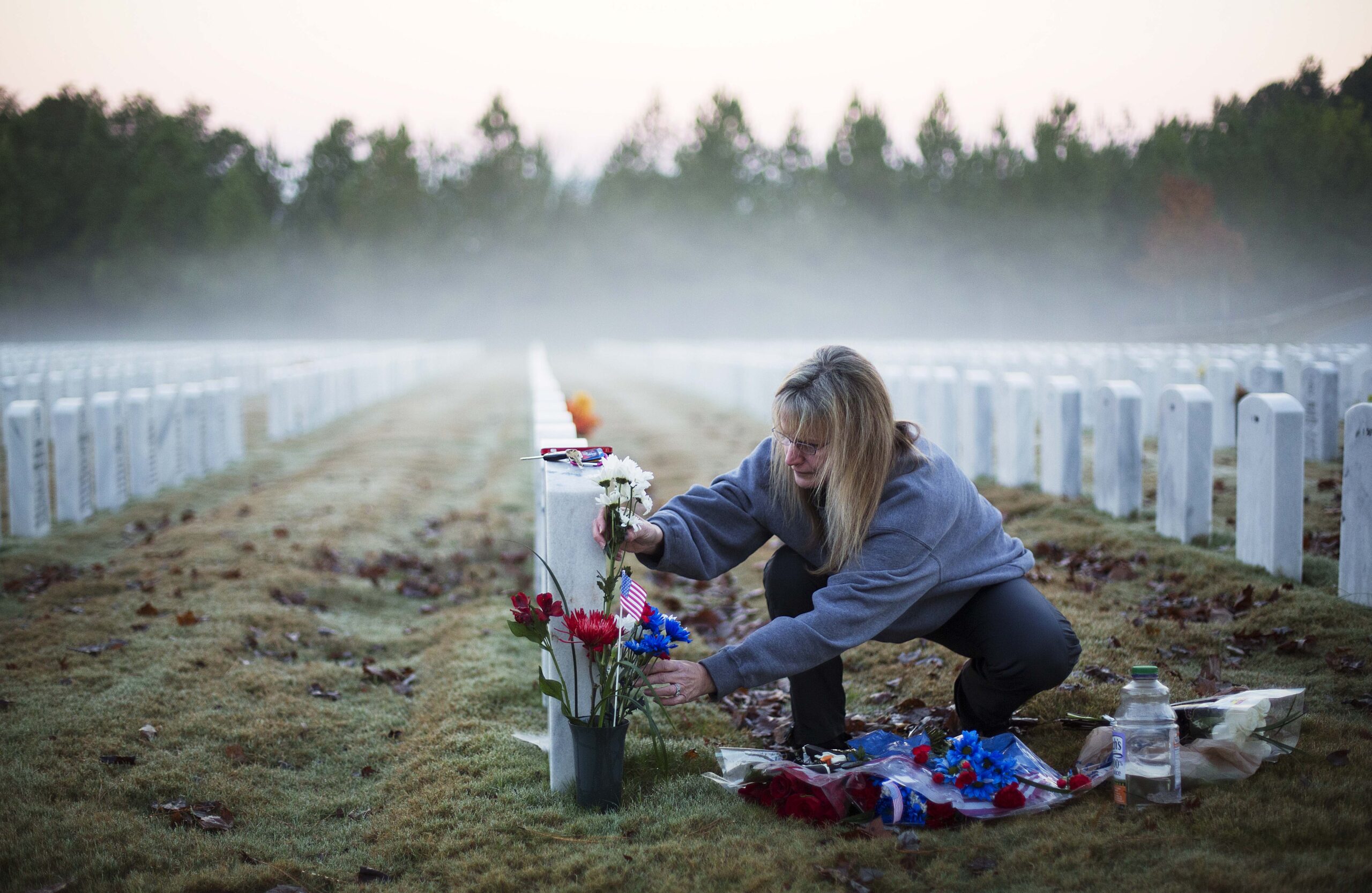A woman places flowers at a military gravestone in a cemetery