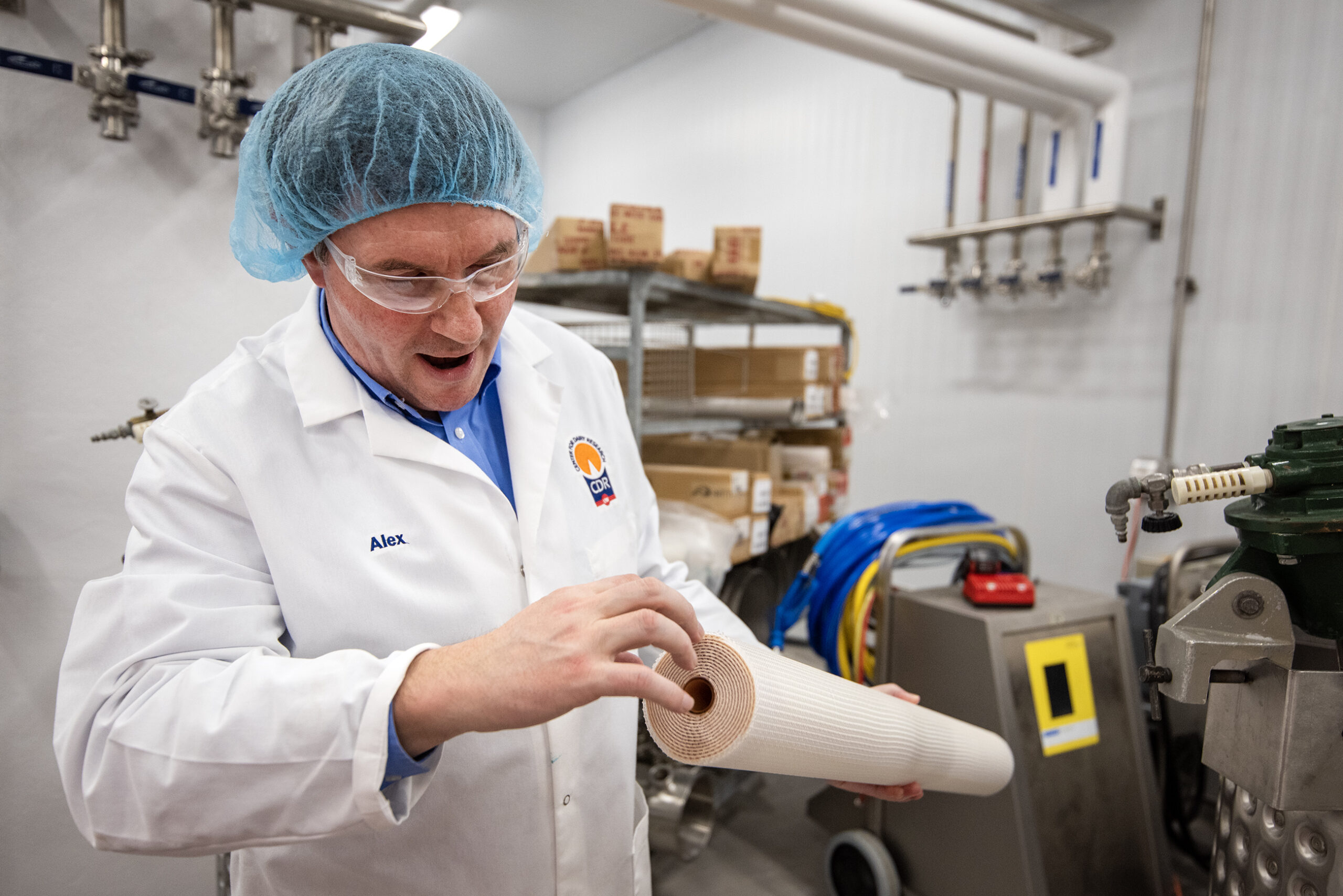 A man with a hairnet and a lab coat holds a roll of white material in a research center.