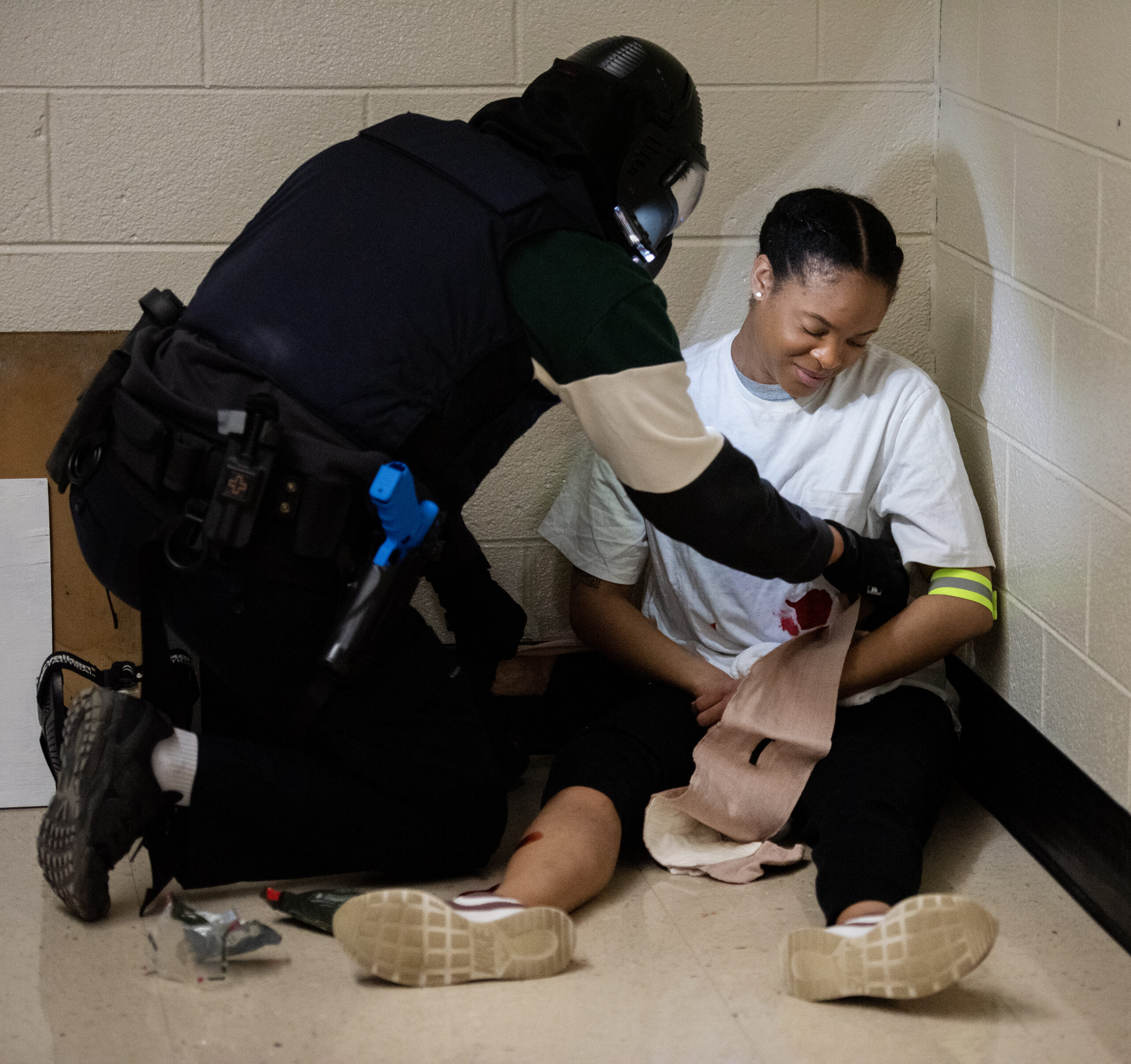 A woman sits on the ground as an officer offers simulated medical aid in while participating in a hands-on training exercise.