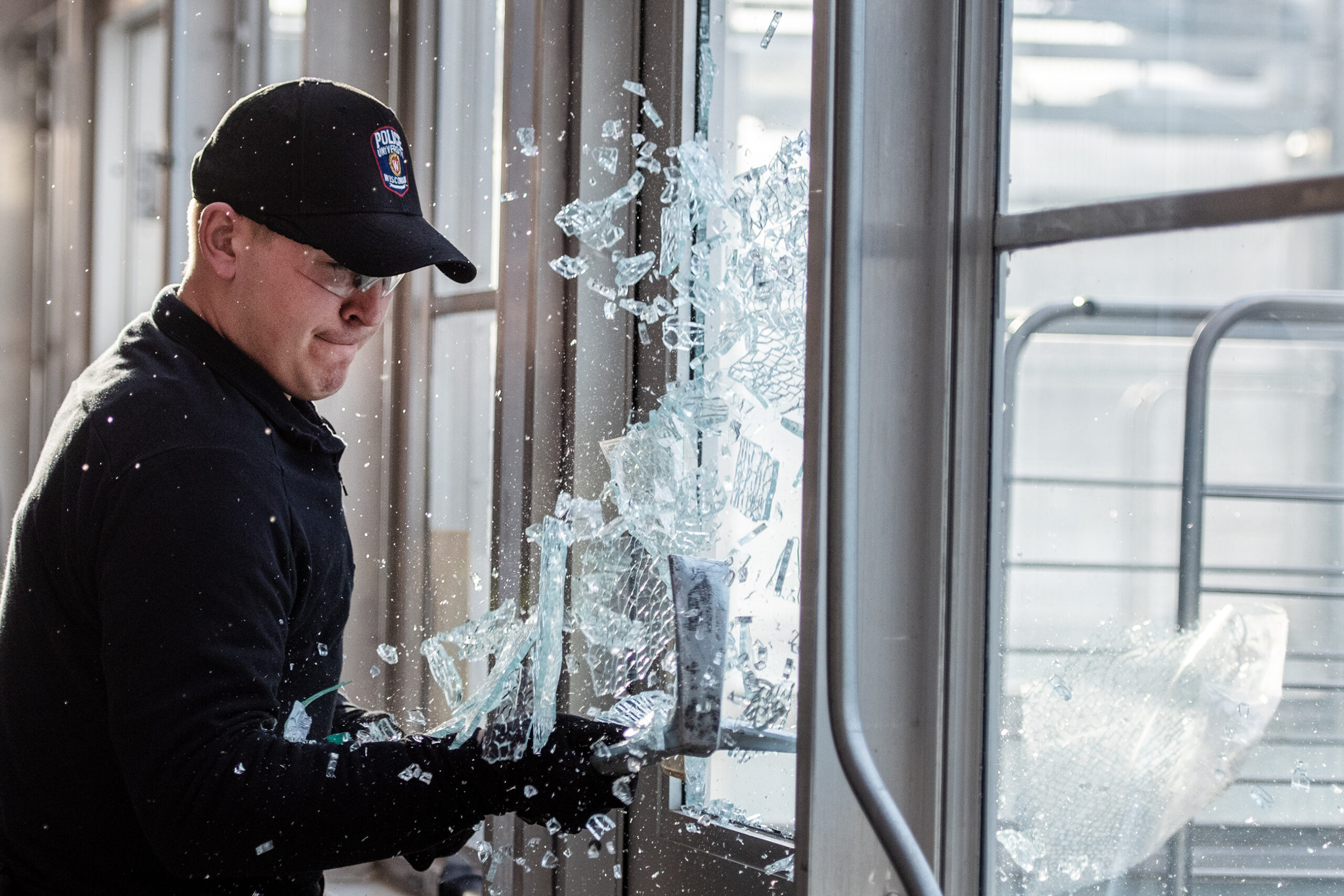 Broken glass flies as an officer uses a tool to break through a door window.