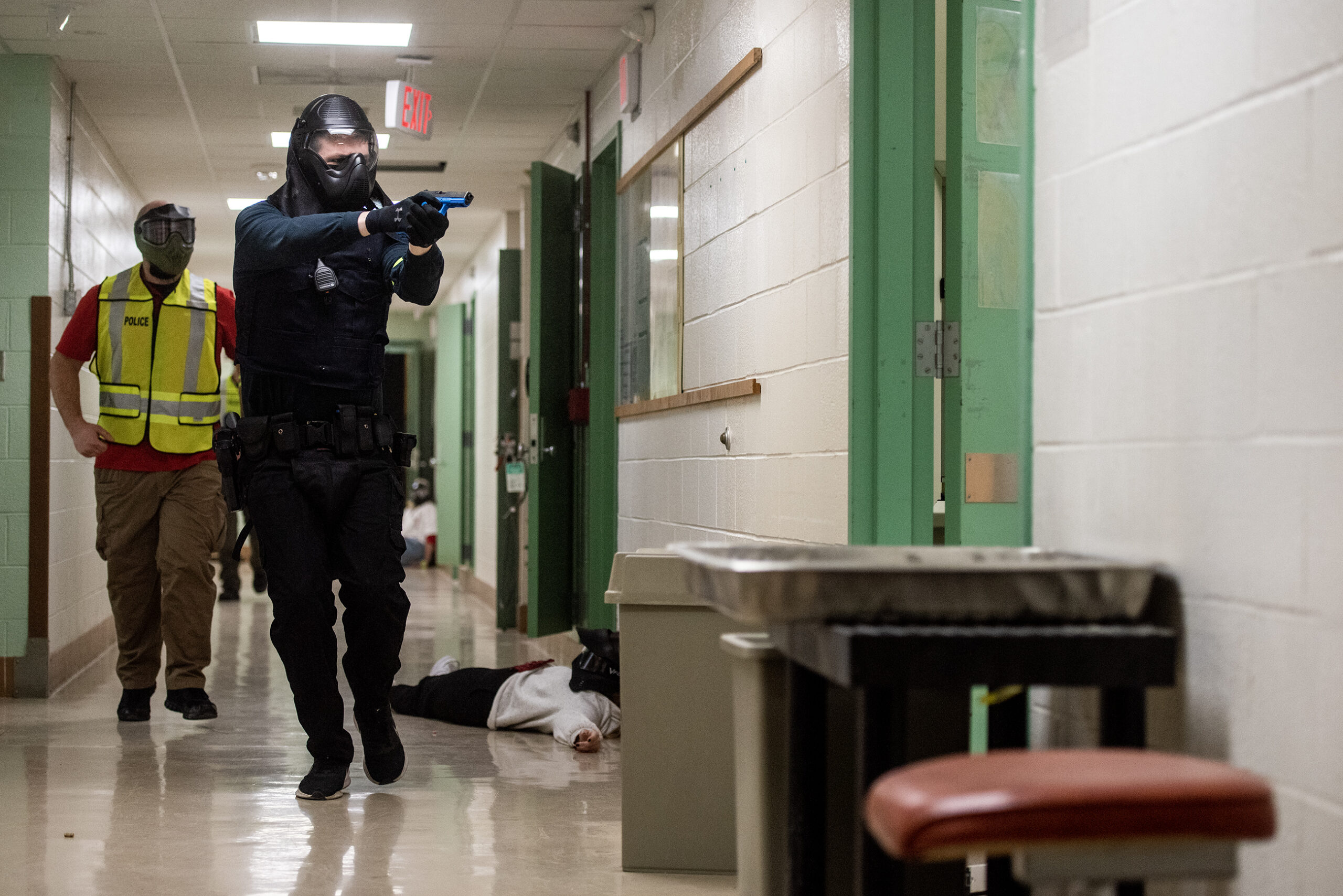 An officer moves through a school hallway holding a fake weapon during a simulated training exercise.