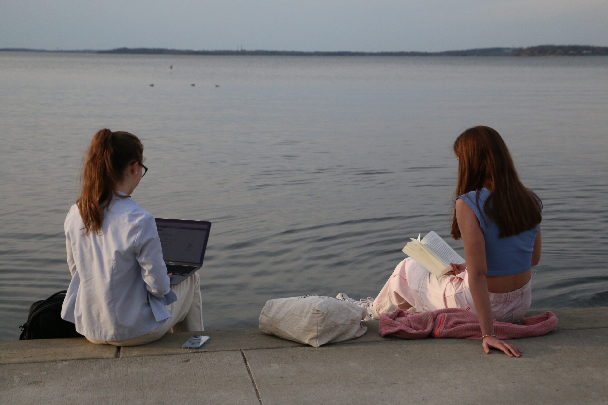 Two college students sit with their laptops and schoolwork by the lake