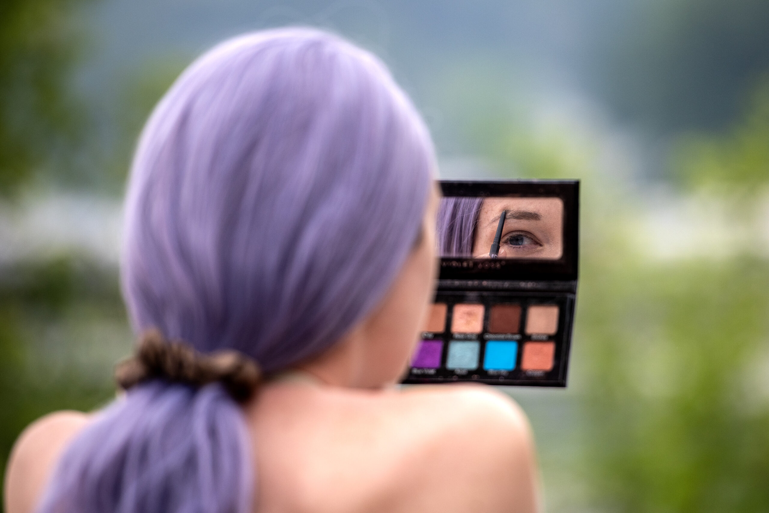 Echo holds an eyeshadow palette as they apply makeup.