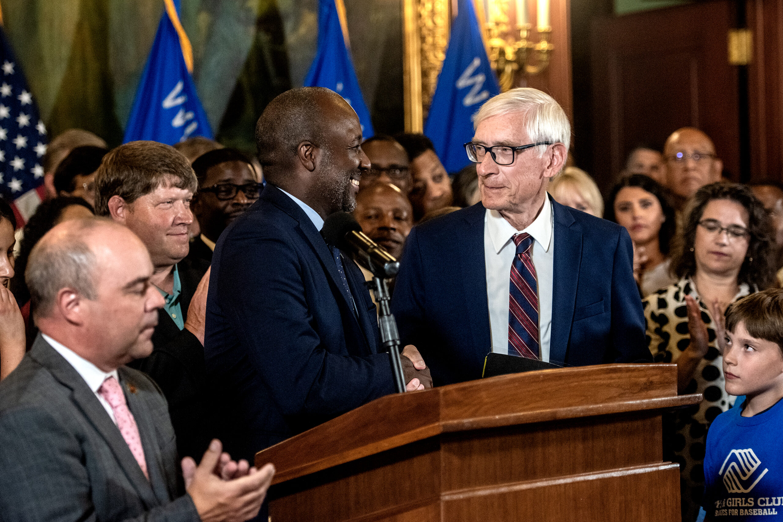 Gov. Evers shakes hands with an official before he speaks at a podium.