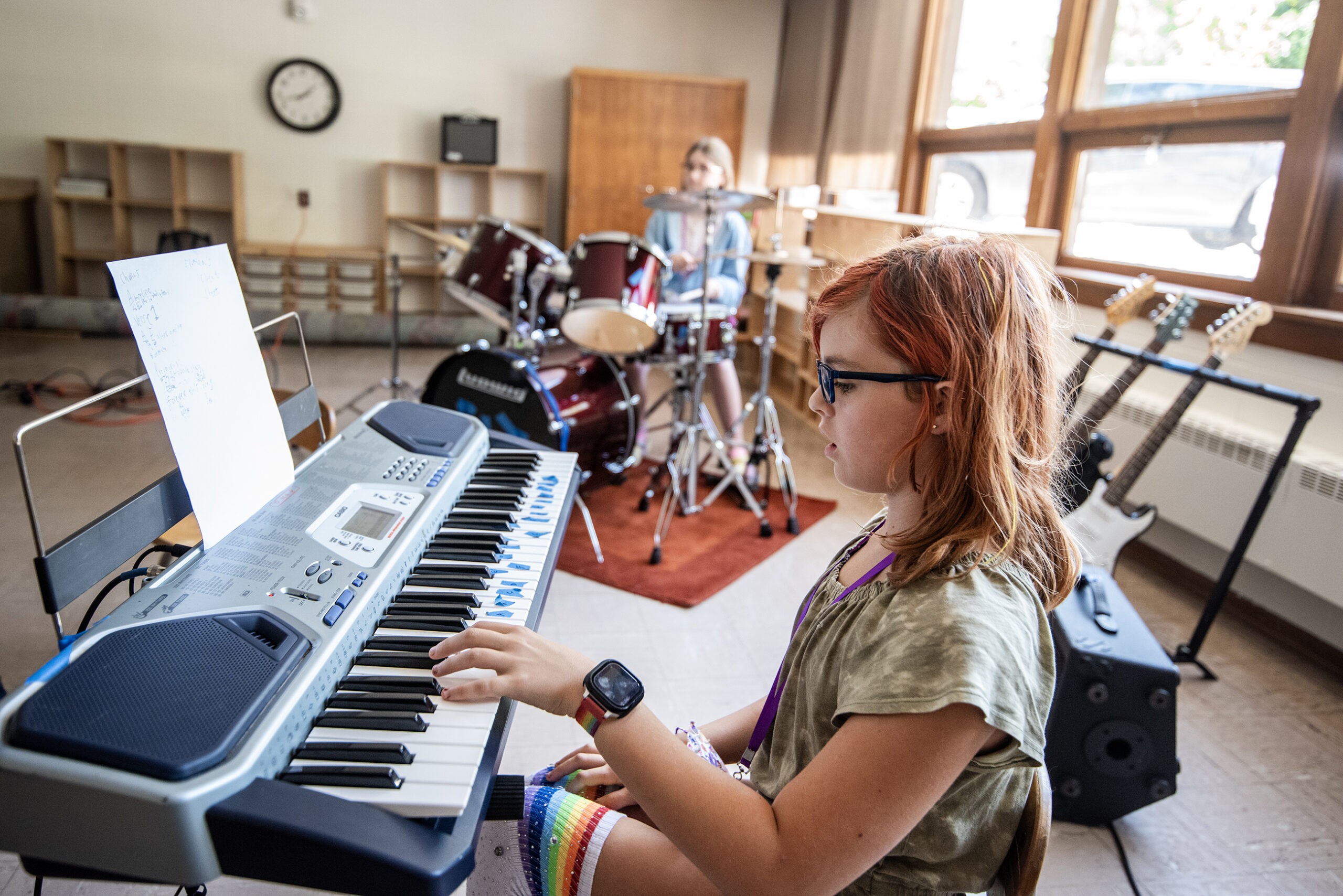 A girl plays the keyboard. A drummer is seen behind her.