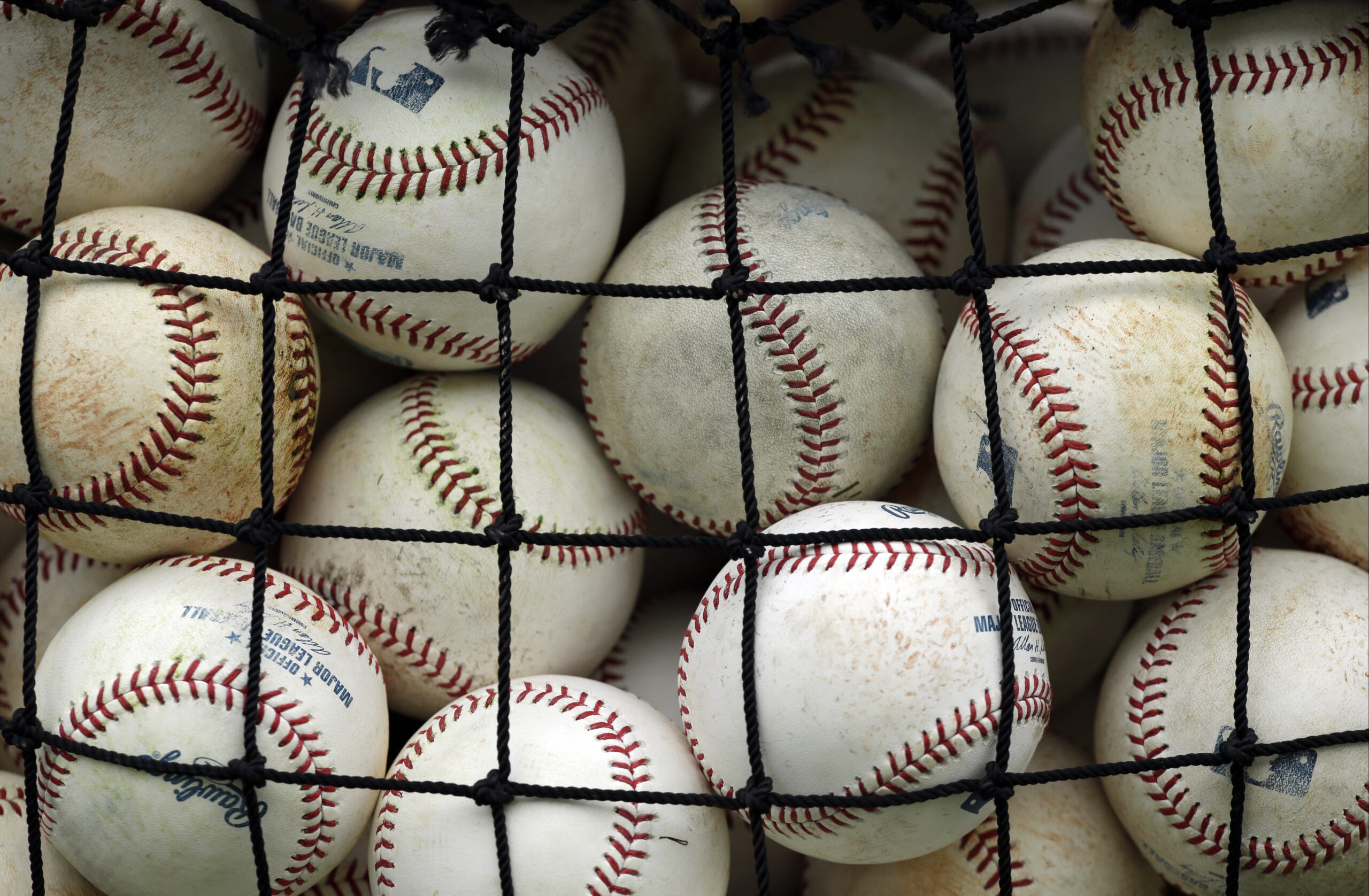 A pile of baseballs sit in a rope net.