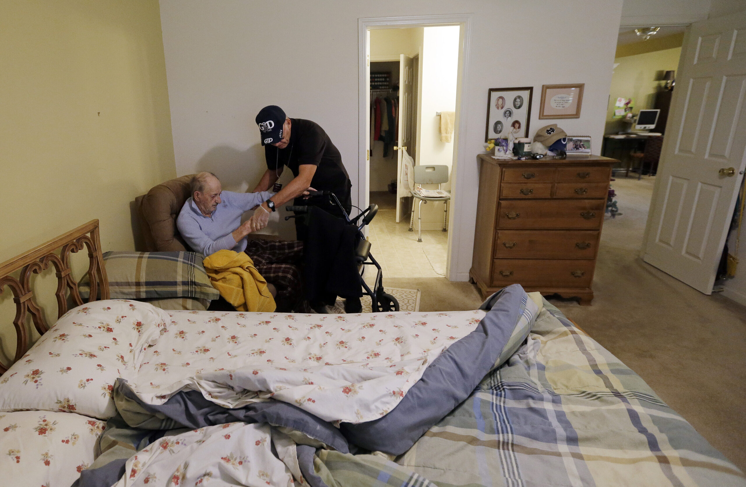 A caregiver helps an elderly person out of a chair