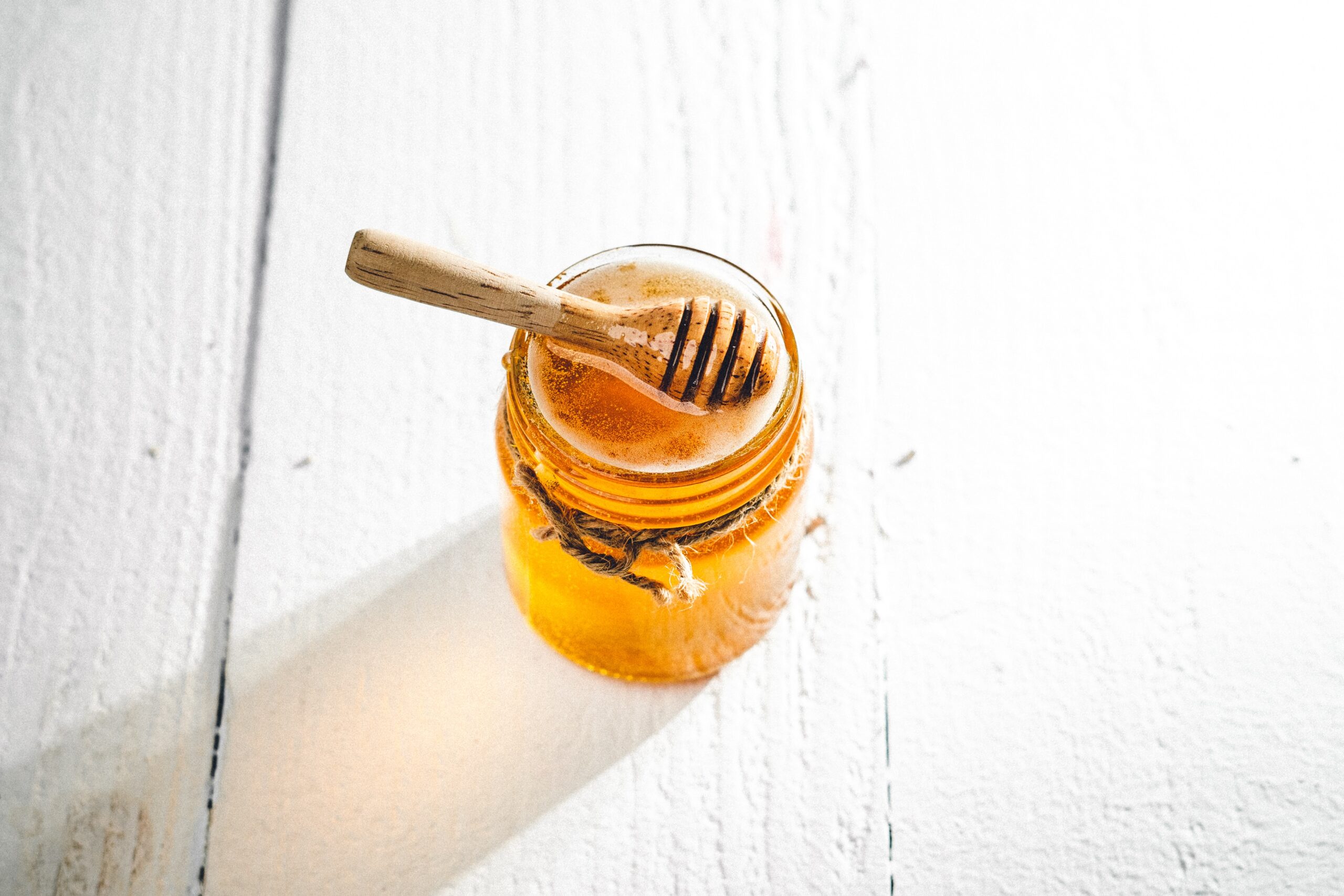 A wooden honey dipper sits atop a clear glass jar filled with honey