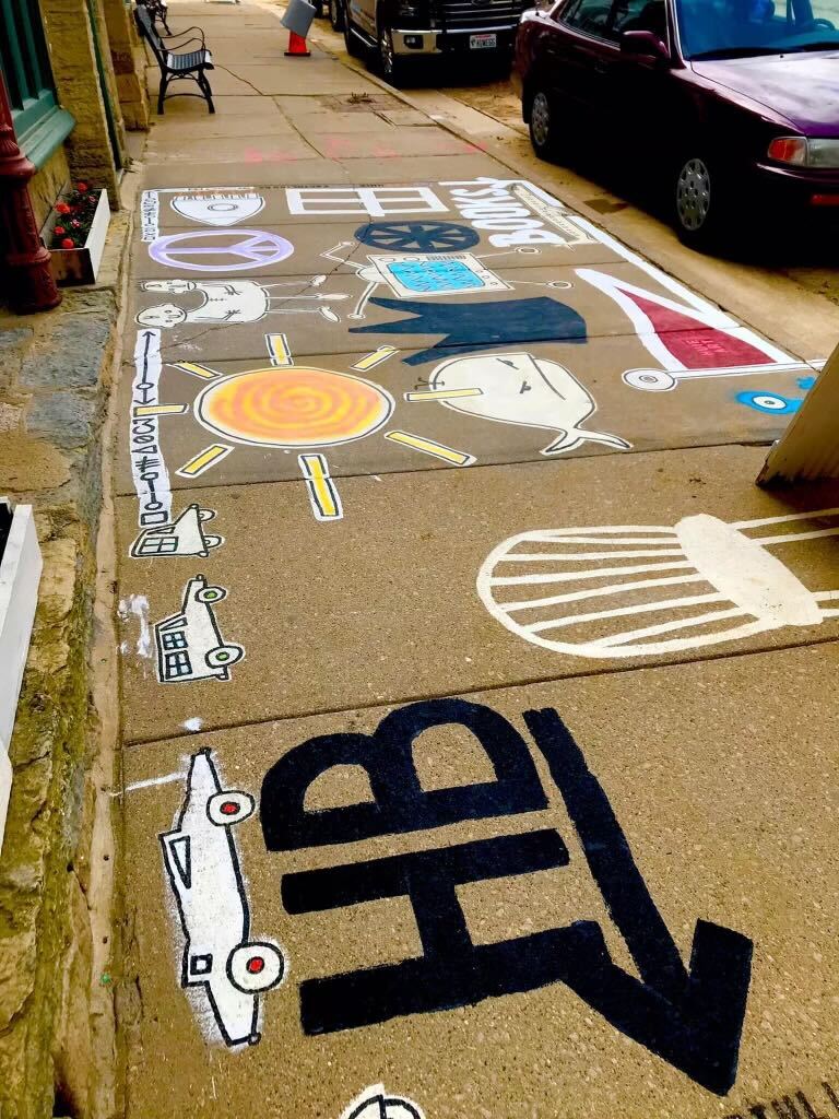 Sidewalk in downtown Mineral Point is painted, with community members' help, featuring a sun, a purple peace sign and animals