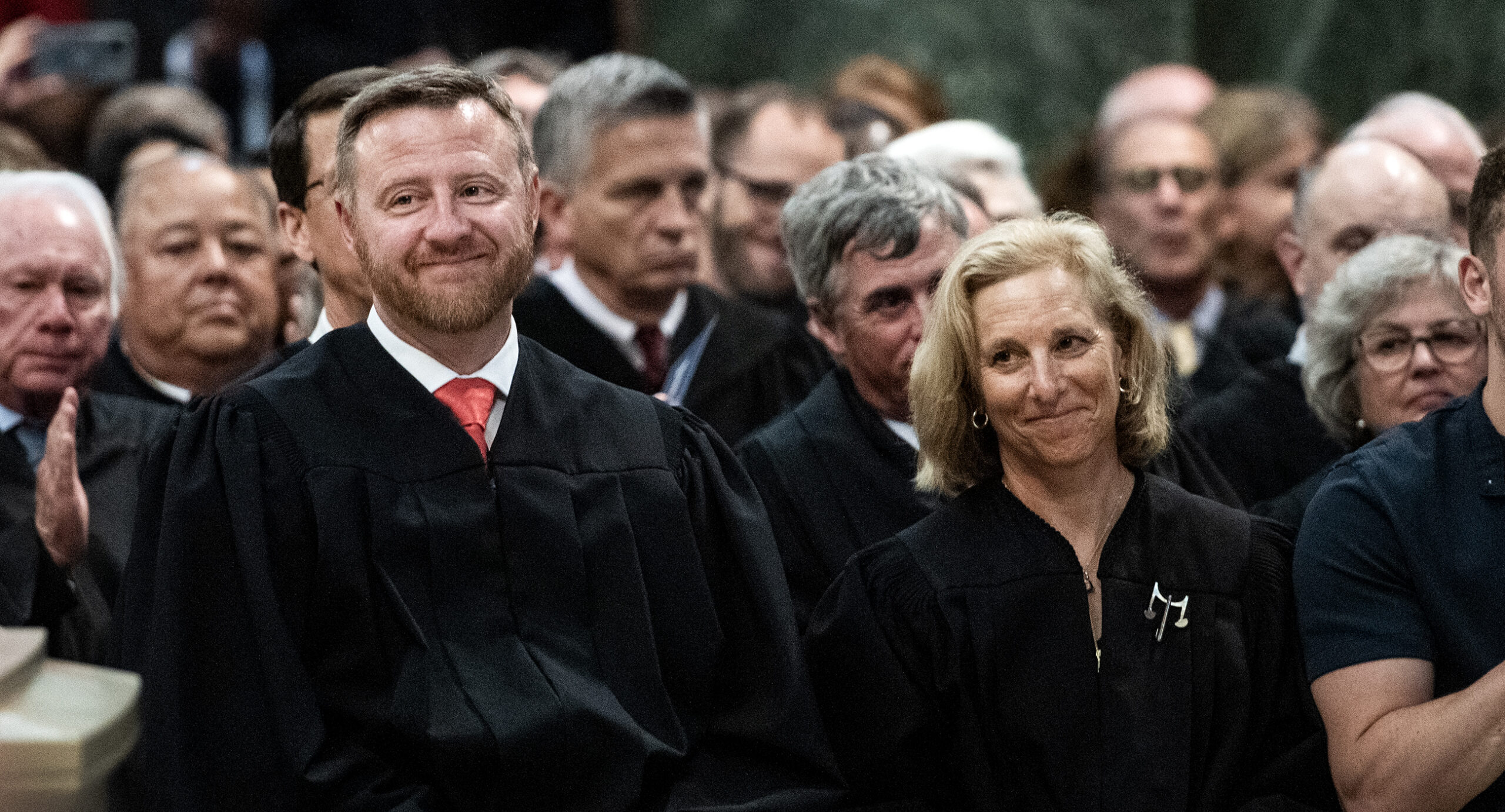 Two justices smile as they sit together in a crowd.