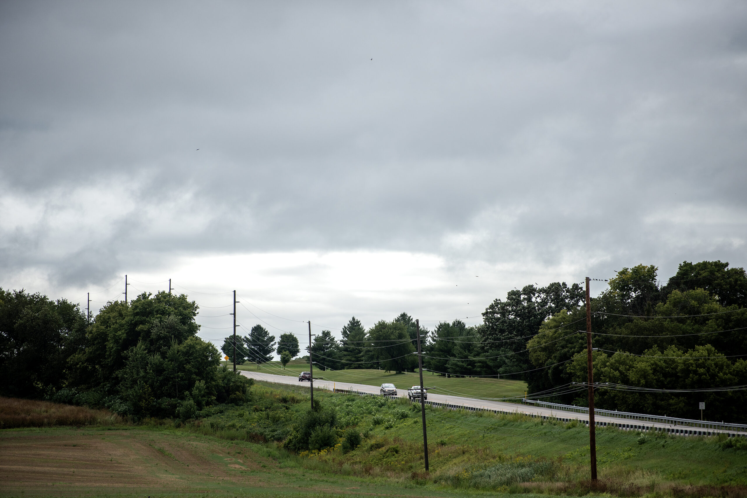 Dark clouds fill the sky as cars pass by on a county highway.