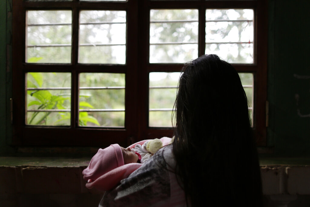 A woman holds baby in hands looking out the window