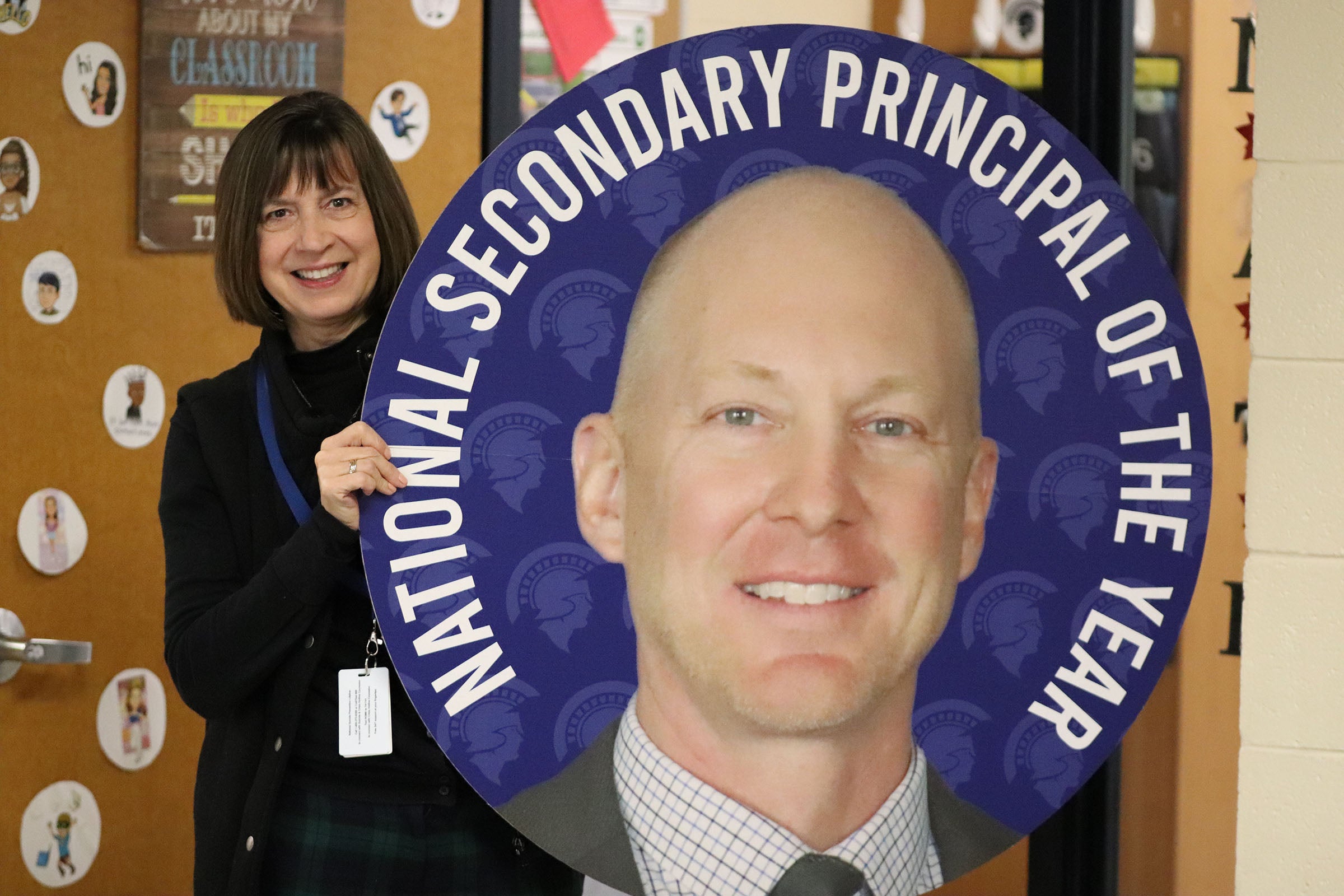 A teacher holds a sign with Principal Andrew Farley's face on it, with writing that says he's the national principal of the year