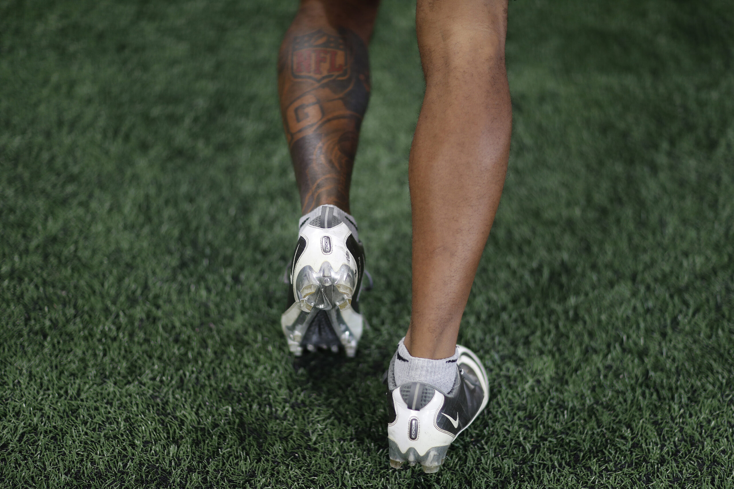 The back of the legs of a football player stepping in turf as he warms up.