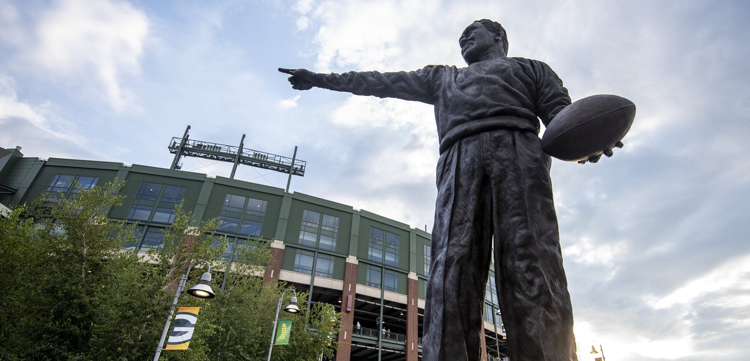 A statue of a man holding a football with his arm outstretched is seen in front of Lambeau Field.