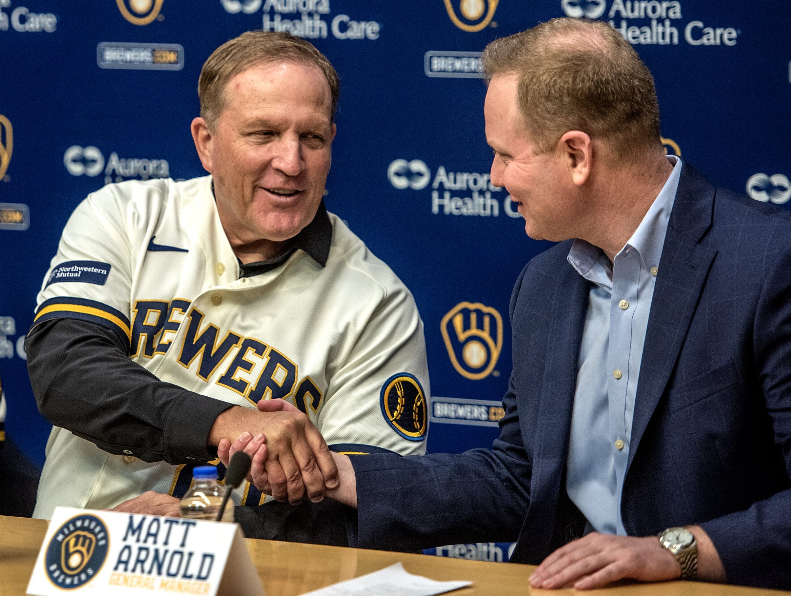Pat Murphy wears a Brewers jersey as he leans over to shake hands with the general manager.