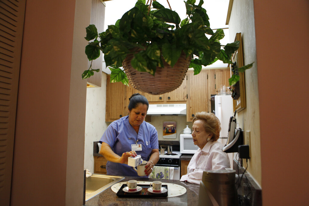 In this photo taken Friday, Sept. 3, 2010, home health aide Maria Fernandez, left, makes coffee for Herminia Vega, 83, right, as she performs household chores for Vega and her husband.