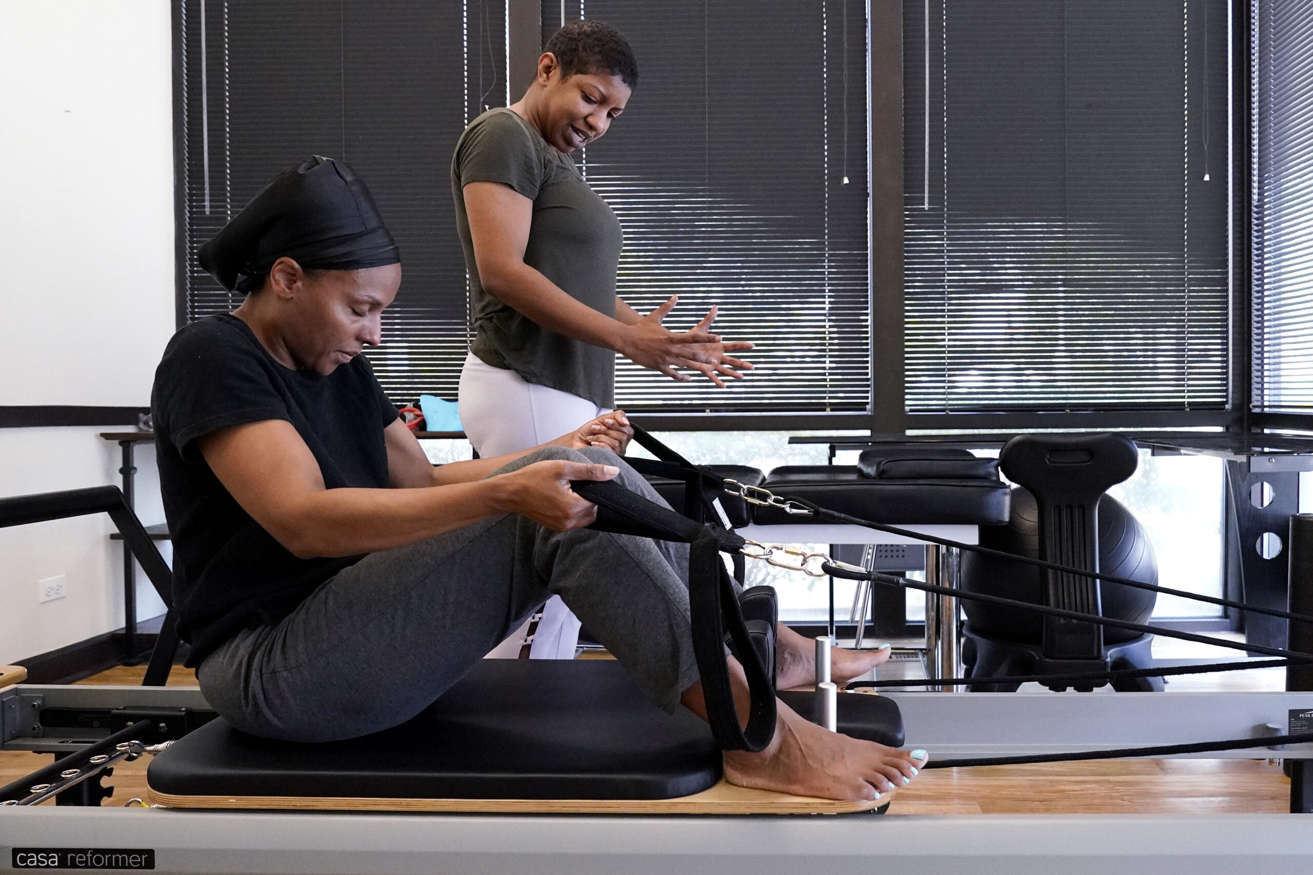 An instructor helps a patient do a Pilates exercise on a machine with cables.